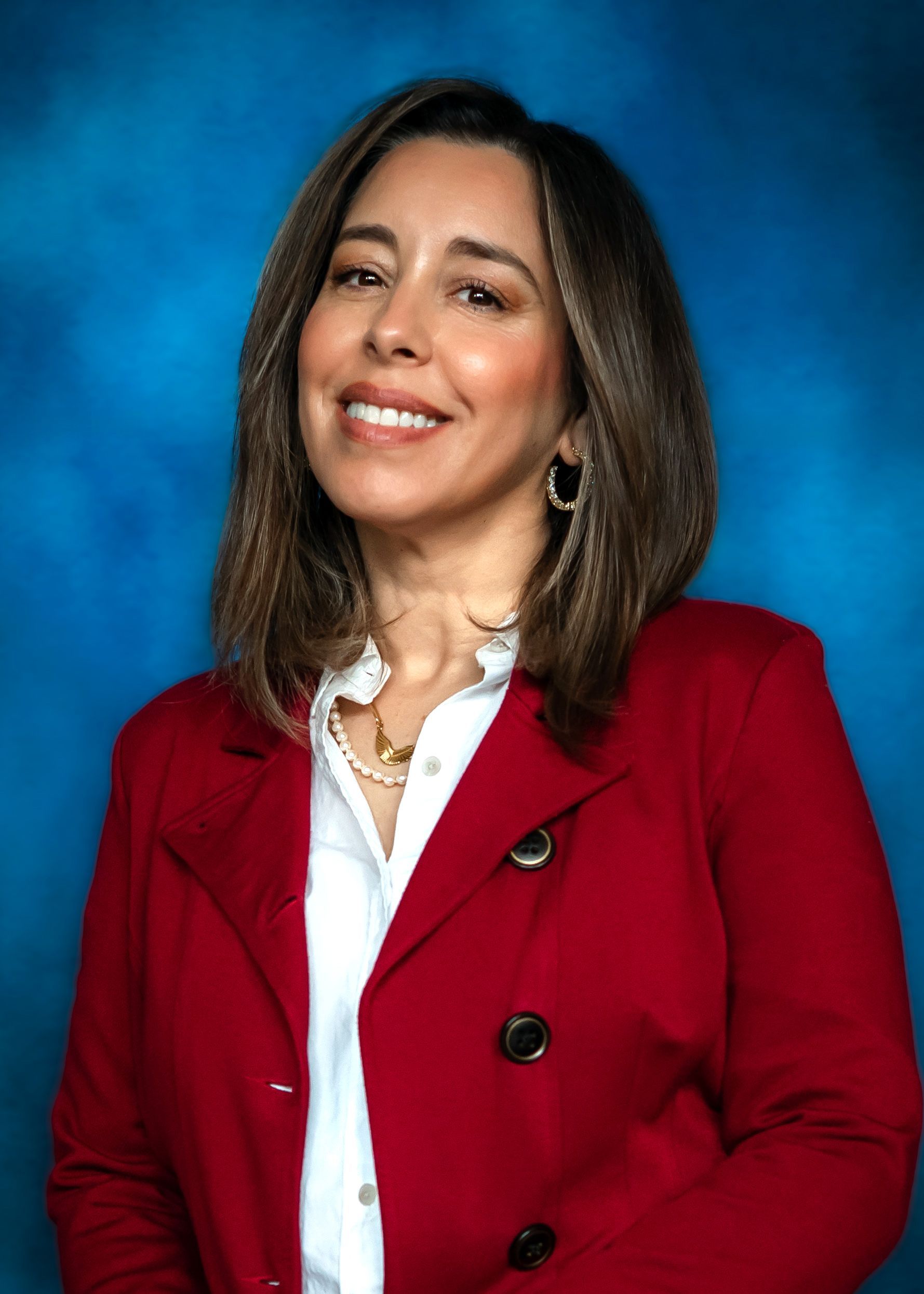 Woman with medium brown hair, wearing a maroon blazer and white blouse, smiling against a blue backdrop.