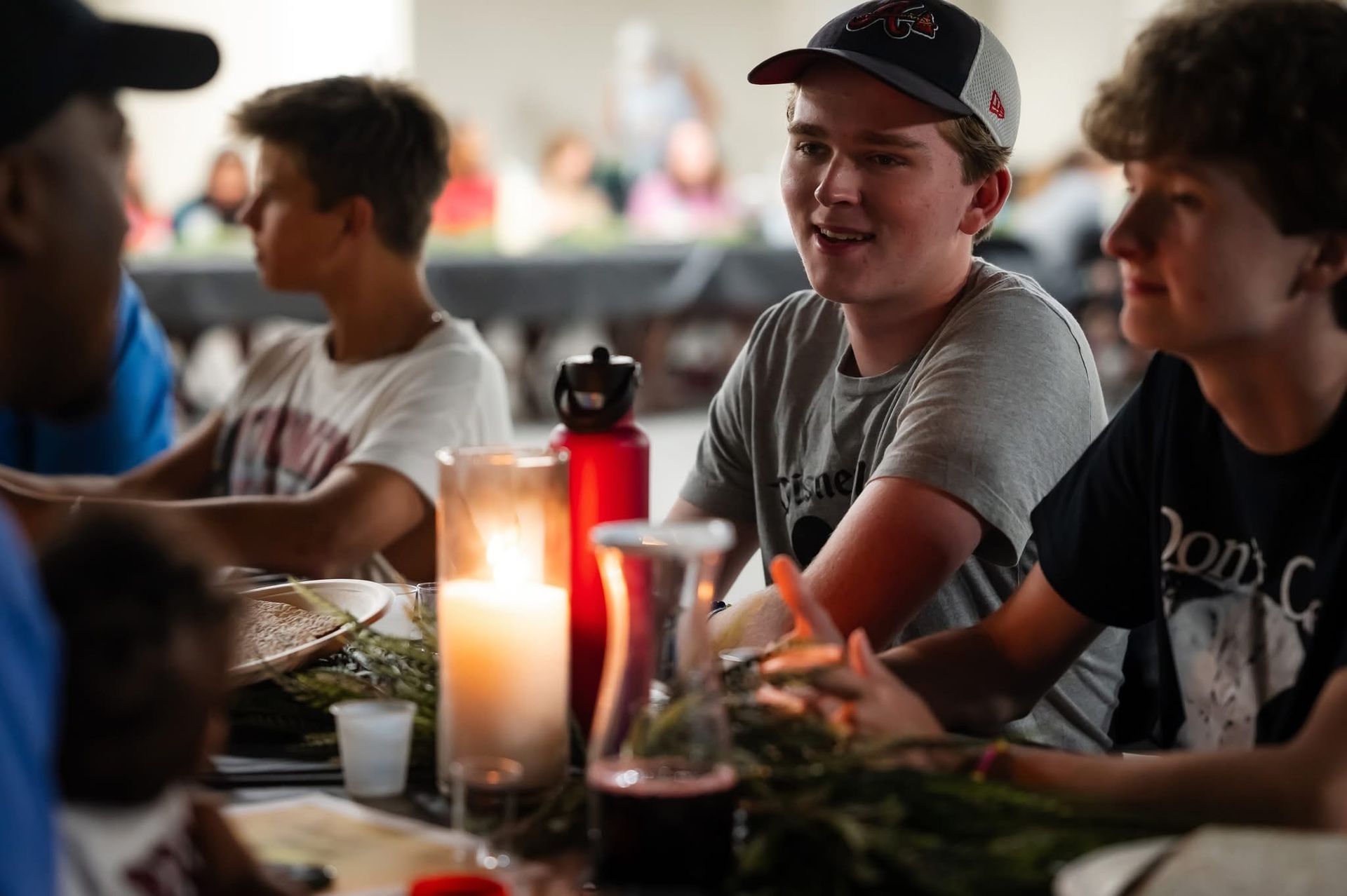 People at a candlelit table, conversing. One wears a cap and smiles, others listen.