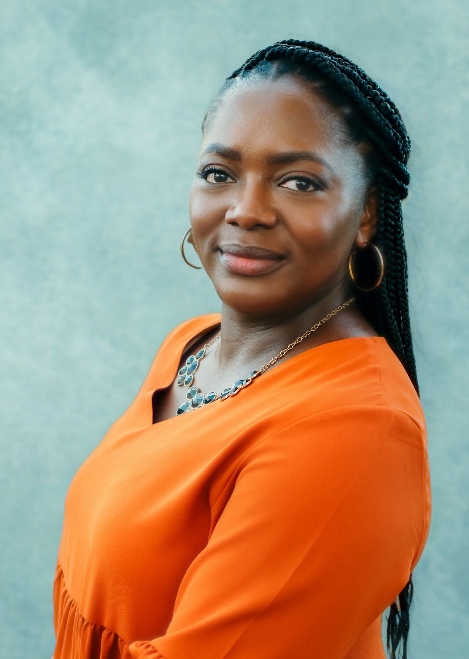 Woman wearing orange shirt, necklace, earrings, and gray background.