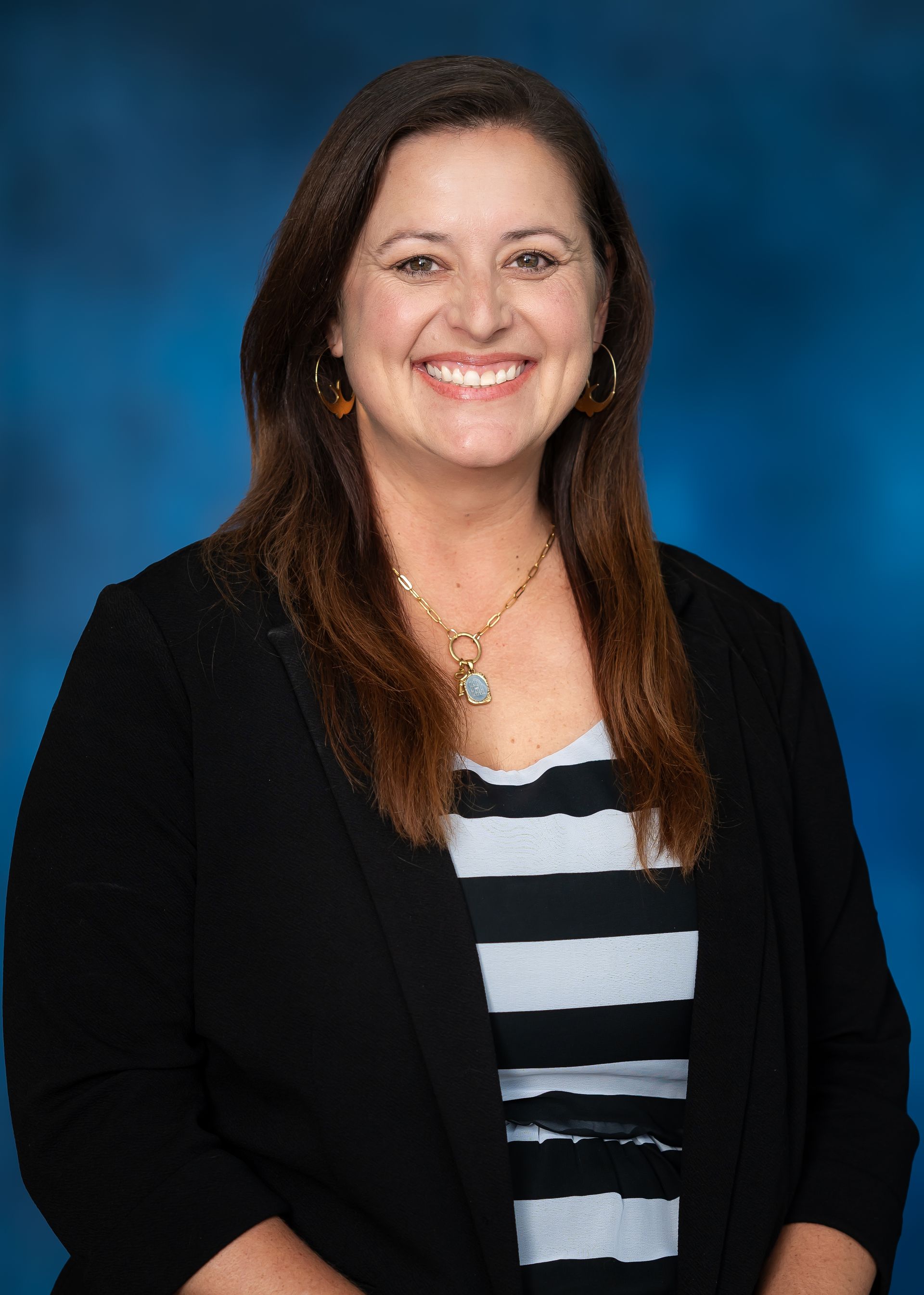Woman in black cardigan, striped shirt, smiling in front of a blue backdrop.