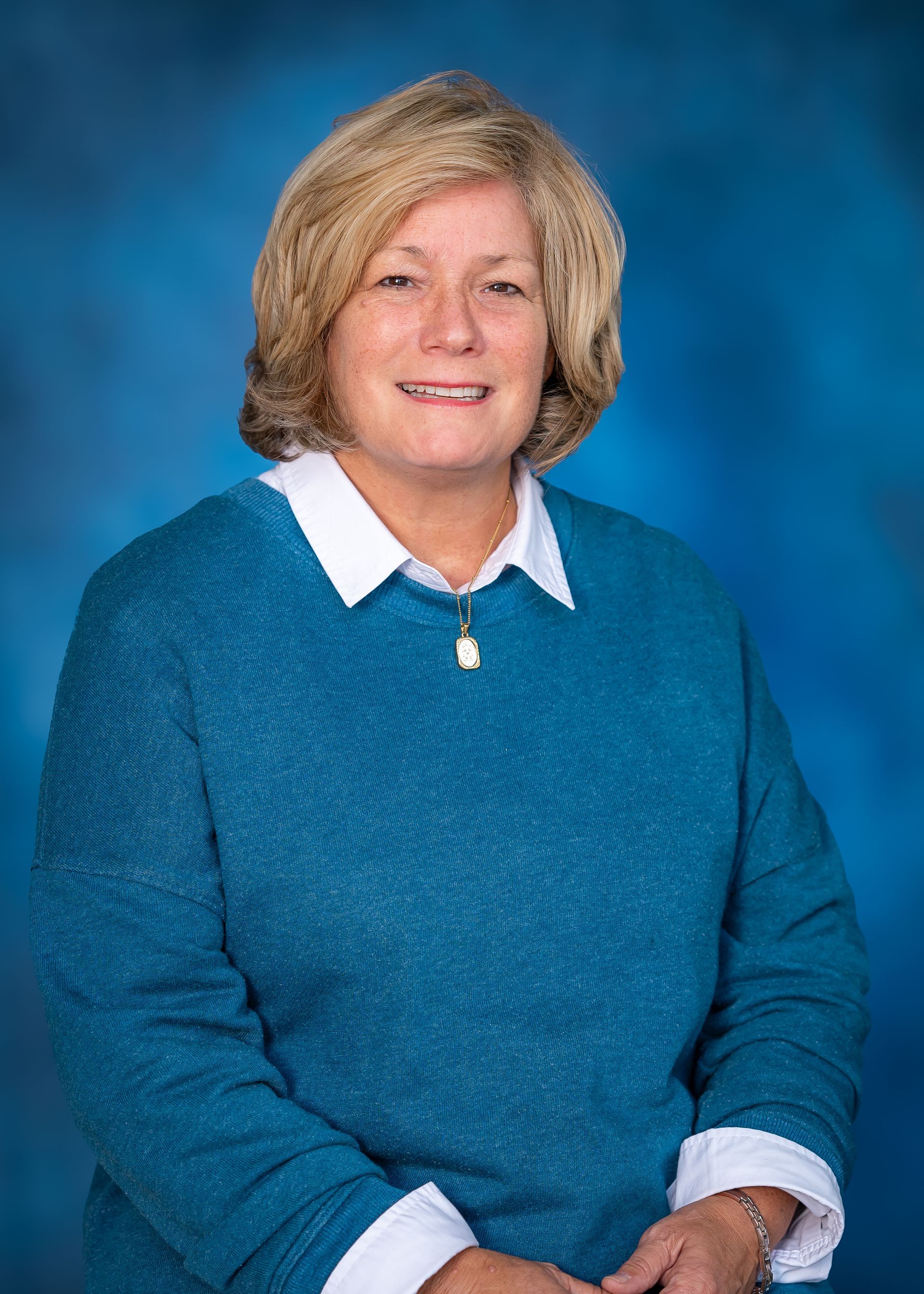 Woman in blue sweater smiles, standing against a blue backdrop.