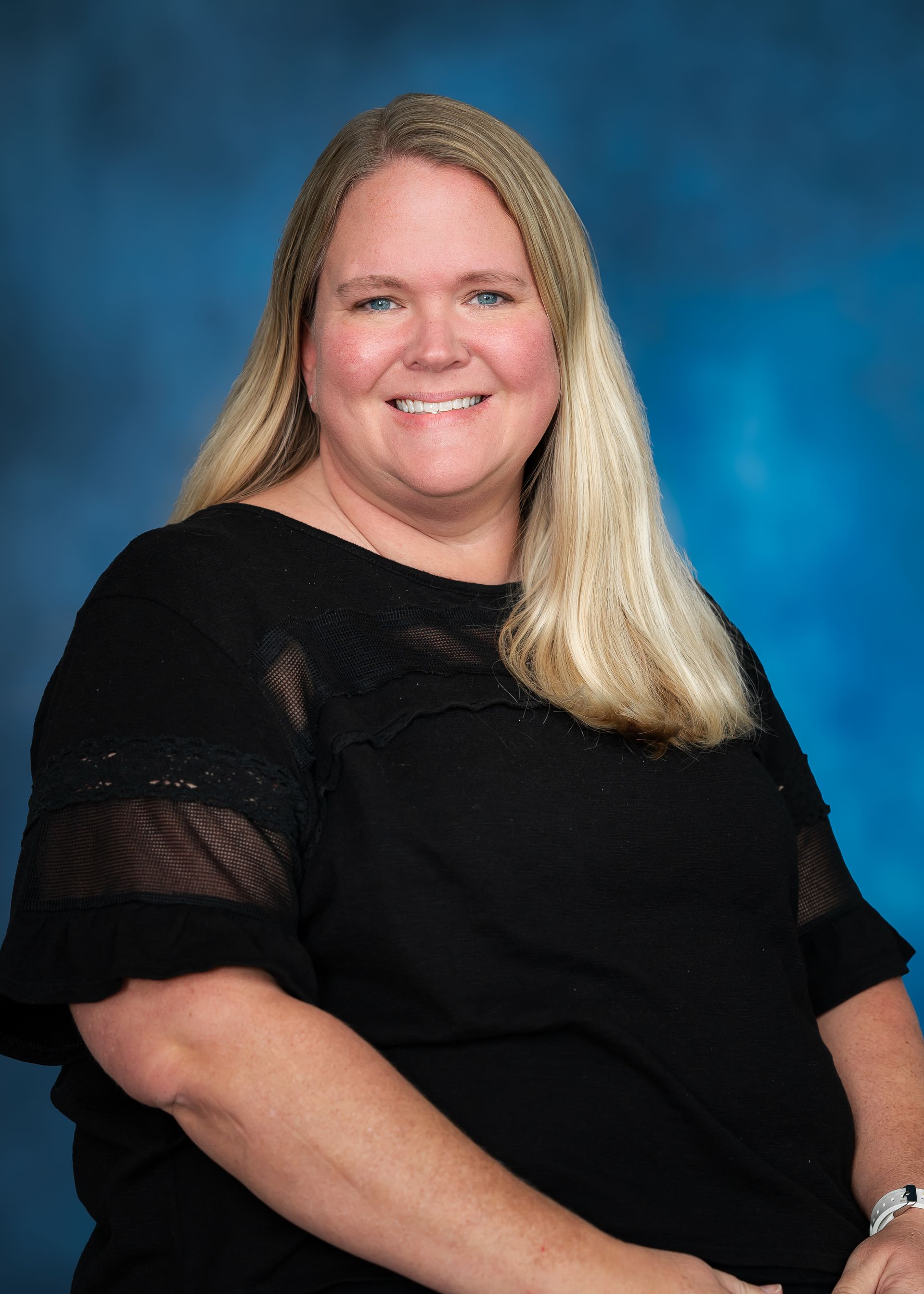 Woman with long blonde hair, smiling, wearing a black shirt, against a blue background.