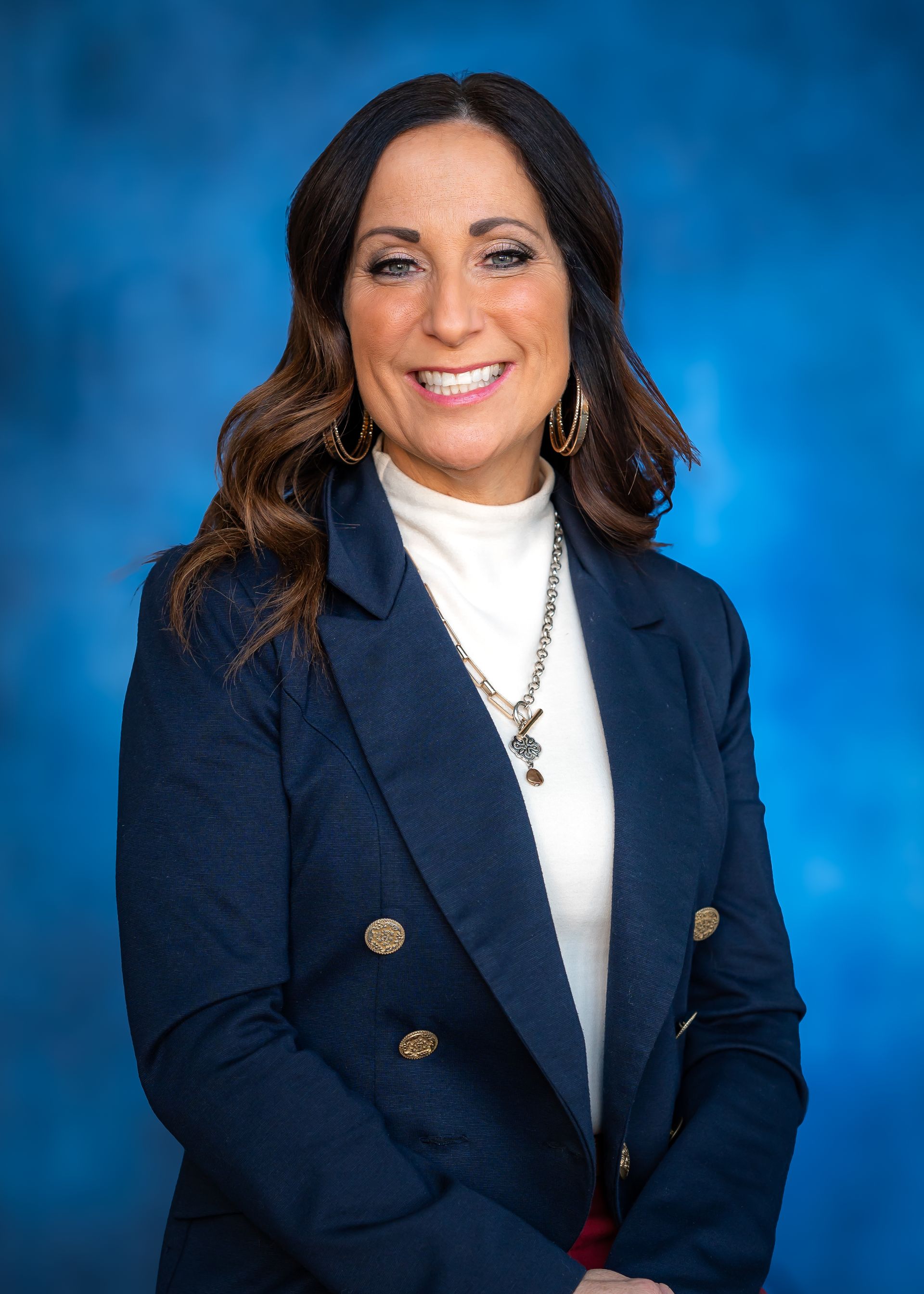 Woman in navy blazer and white turtleneck smiles against a blue backdrop.