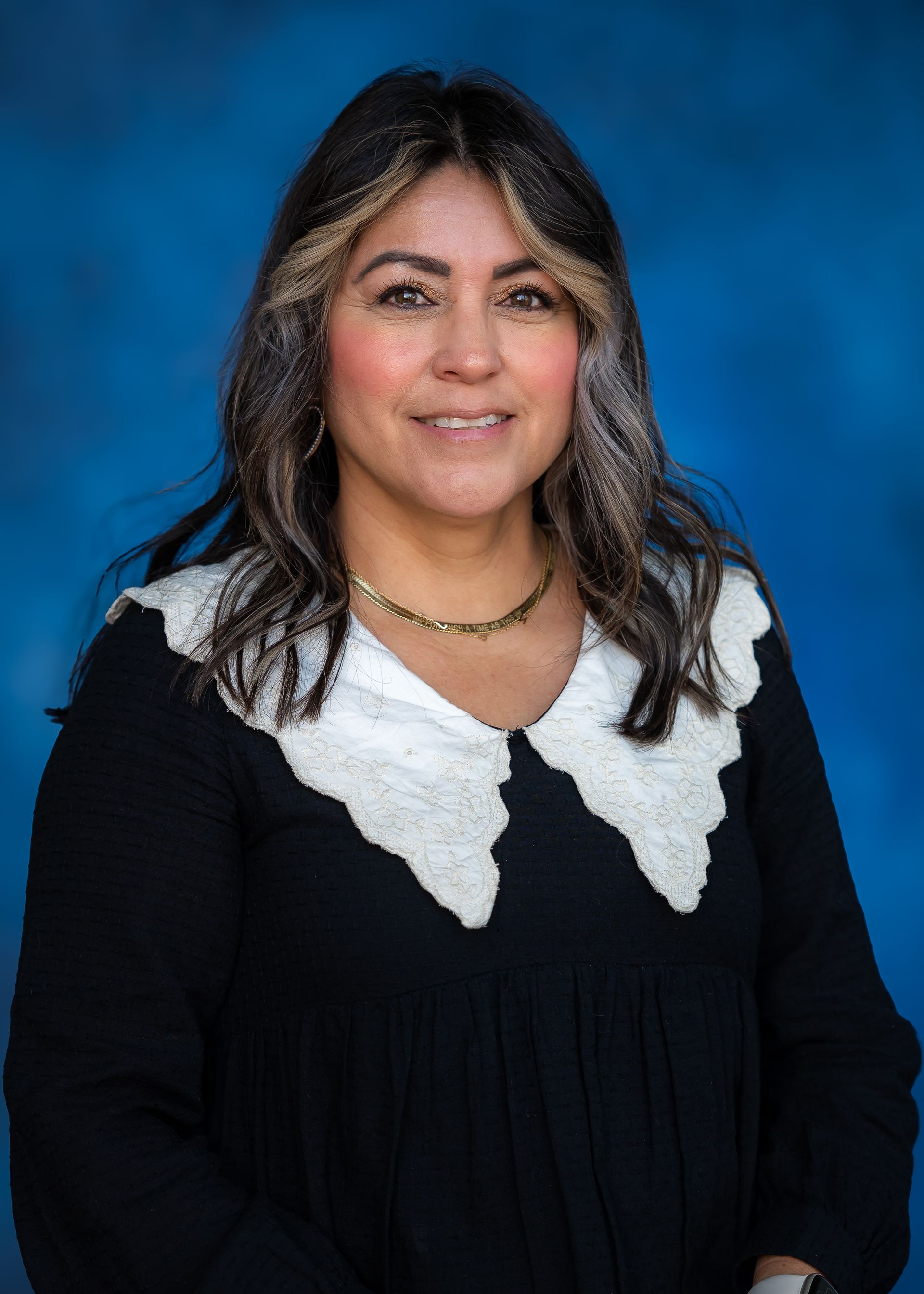 Woman with long dark hair, wearing a black shirt with white scalloped collar, smiling, against a blue background.