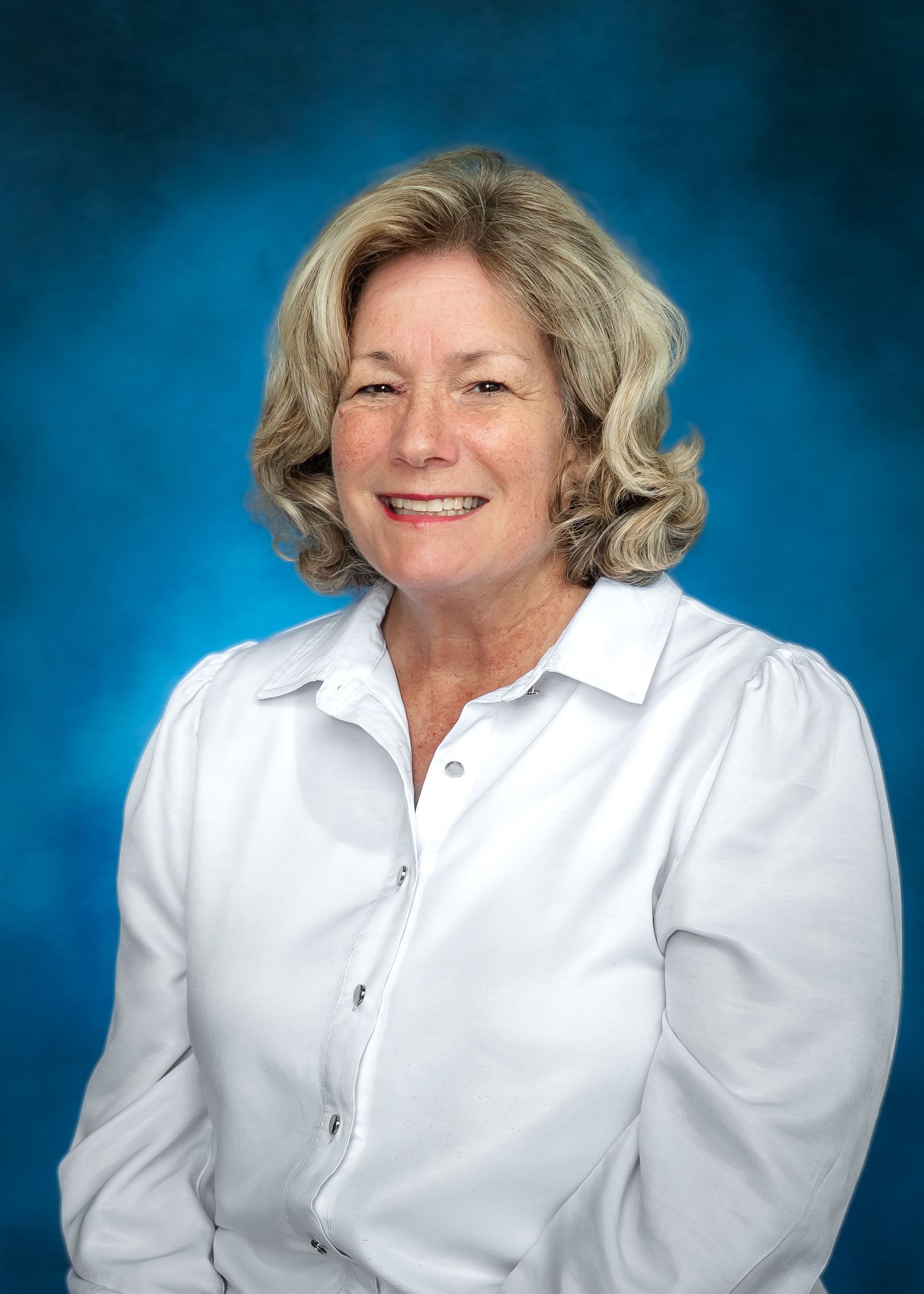 Woman in white shirt smiles, standing against a blue backdrop.