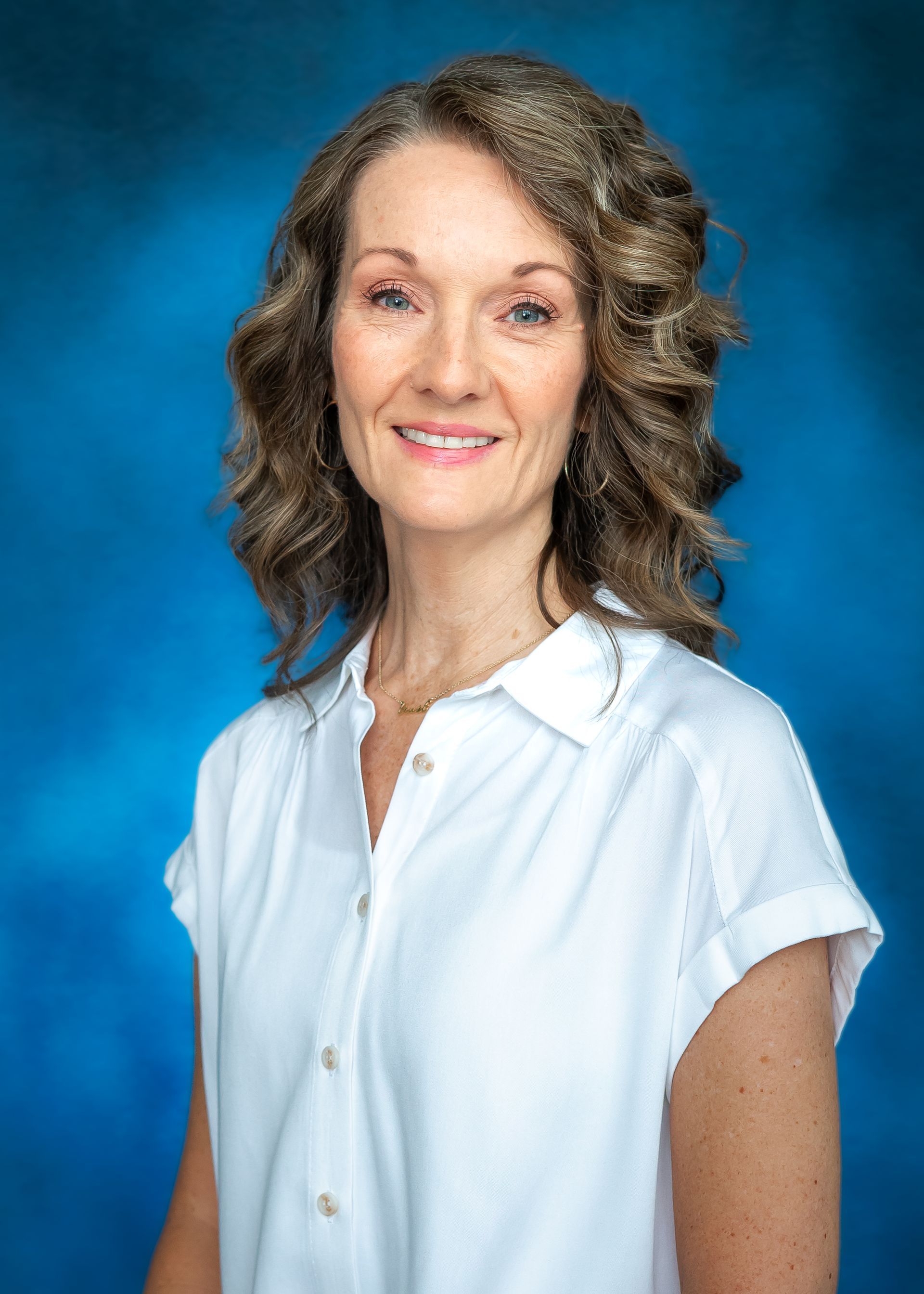 Woman with curly hair in a white top smiling against blue backdrop.