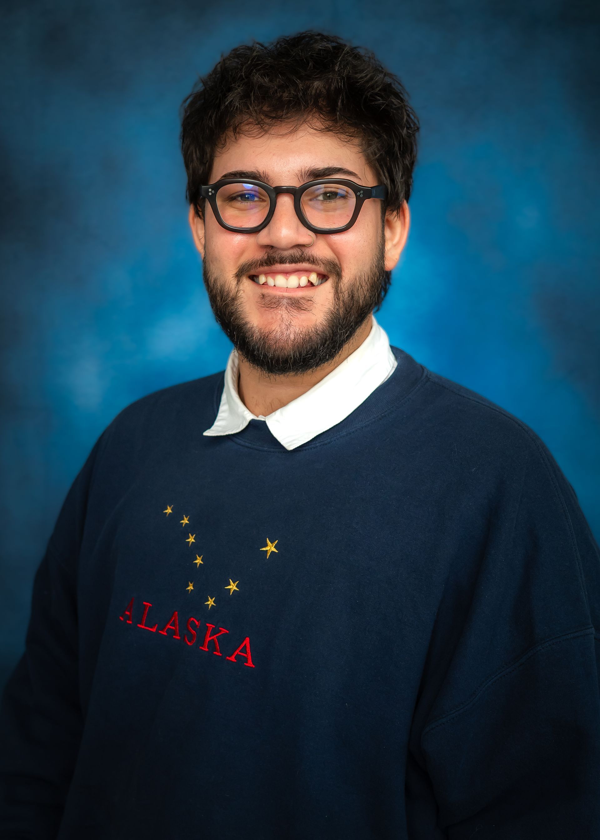 Man with glasses and facial hair, wearing a navy sweatshirt with white collar.
