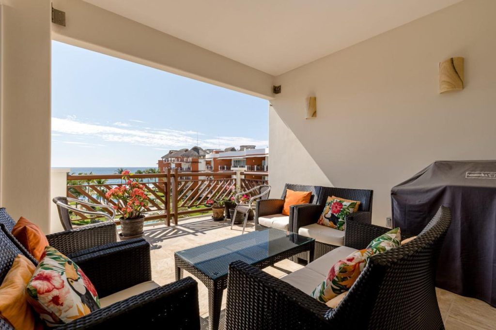 Patio with seating, table, grill, and ocean view behind a wooden railing.