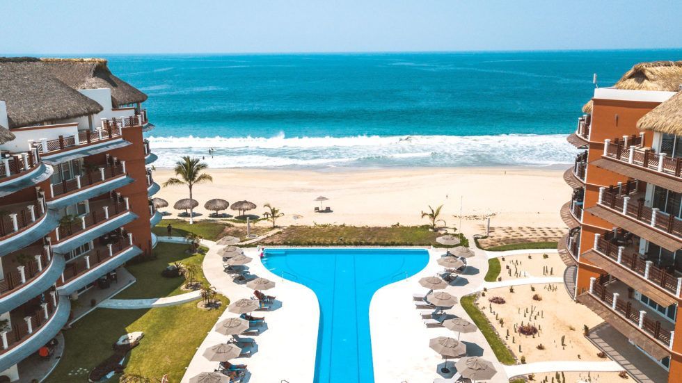 Vivo Resort pool overlooking a beach and ocean. Blue water, sand, and umbrellas.