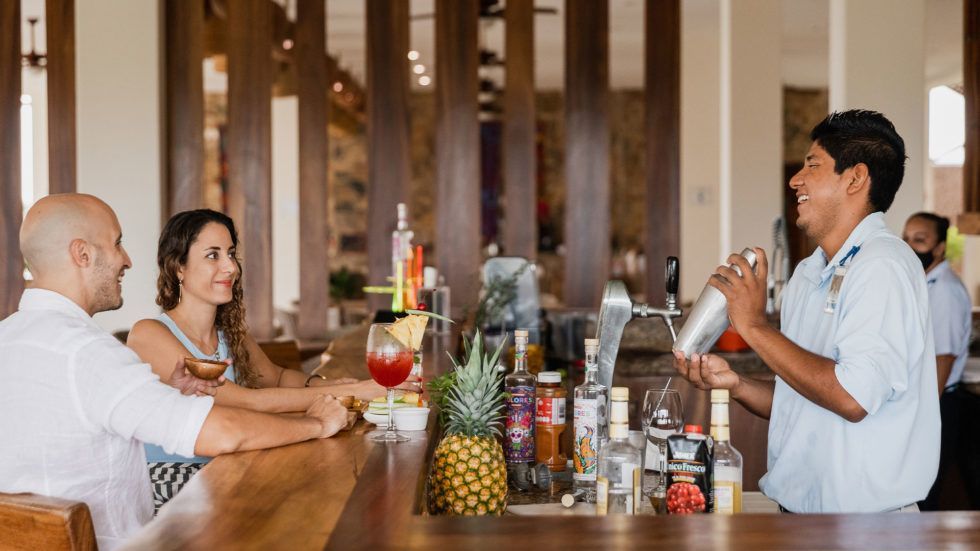 Vivo Resort bartender shaking a cocktail; tropical setting, sunny.