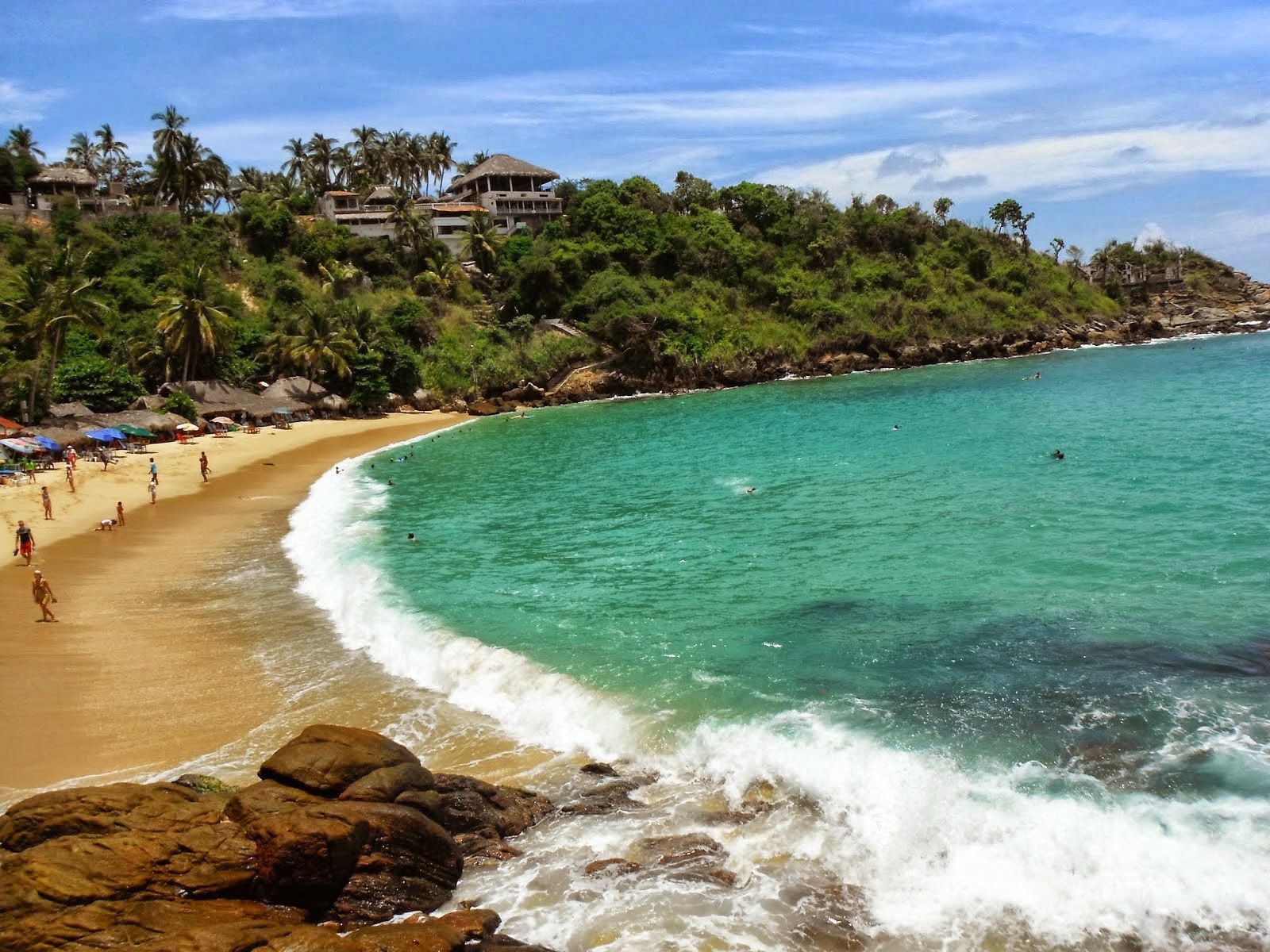 Playa Bococho Beach with turquoise water, golden sand, and lush green hillside under a blue sky.