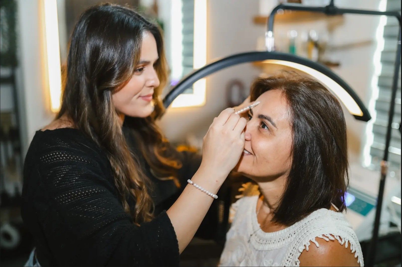 A woman is applying makeup to another woman 's eyebrows in a salon.