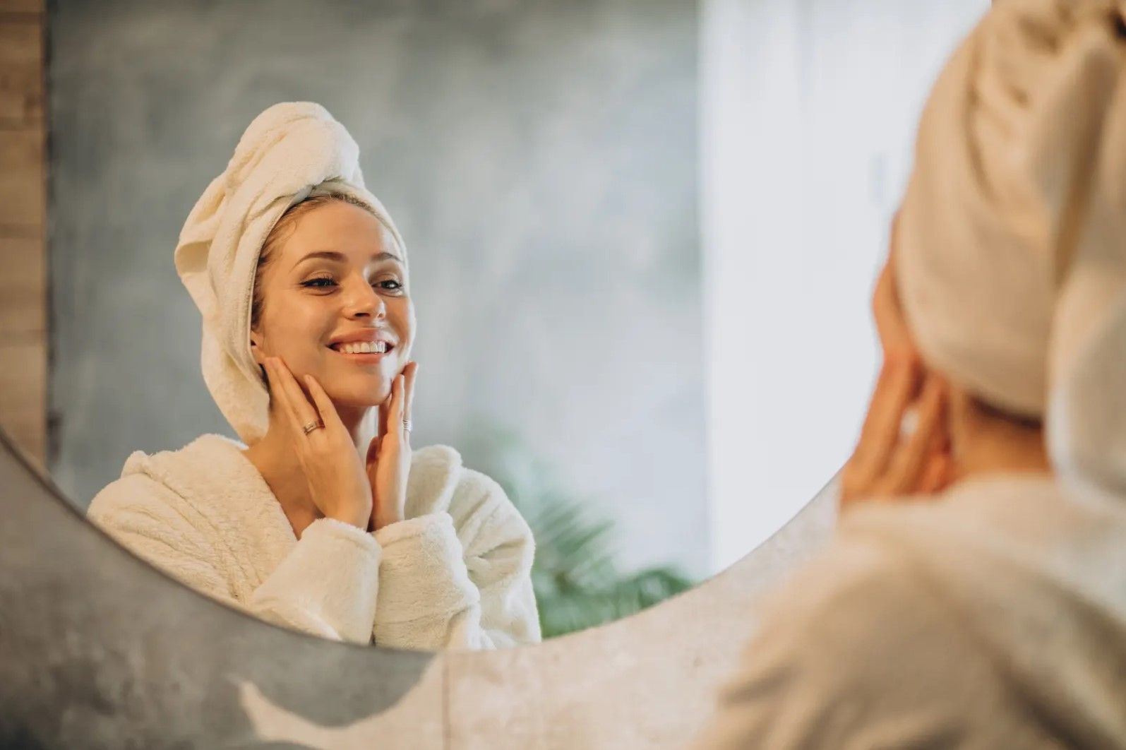 A woman with a towel wrapped around her head is looking at herself in the mirror.