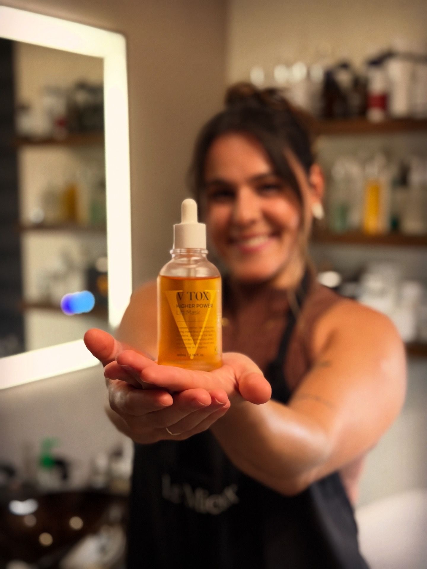 Woman holding up a bottle of yellow liquid. She's smiling in a well-lit space.