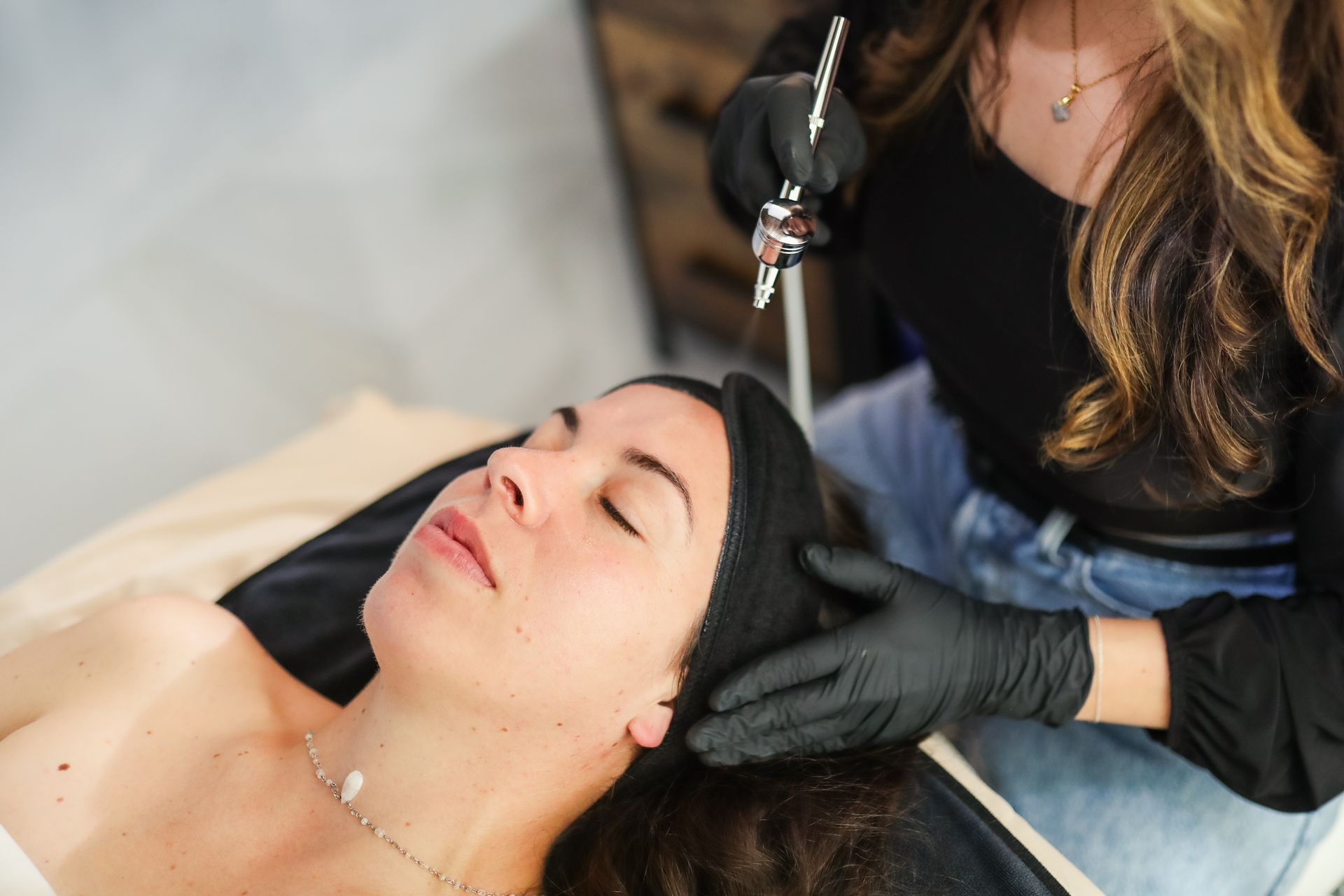 A woman is getting an airbrush treatment on her face.