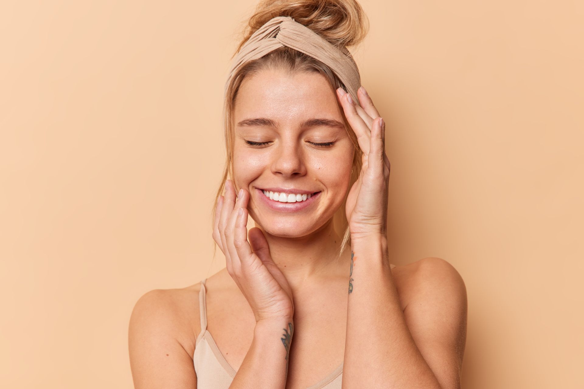 A woman wearing a headband is smiling and touching her face.