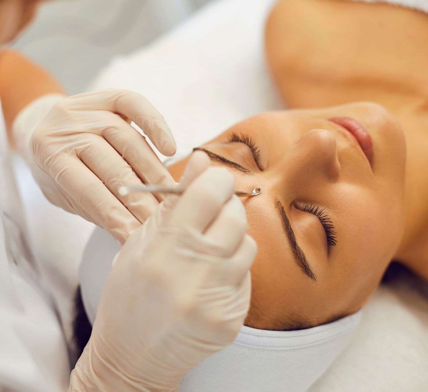 A woman is getting a facial treatment with gloves on. 