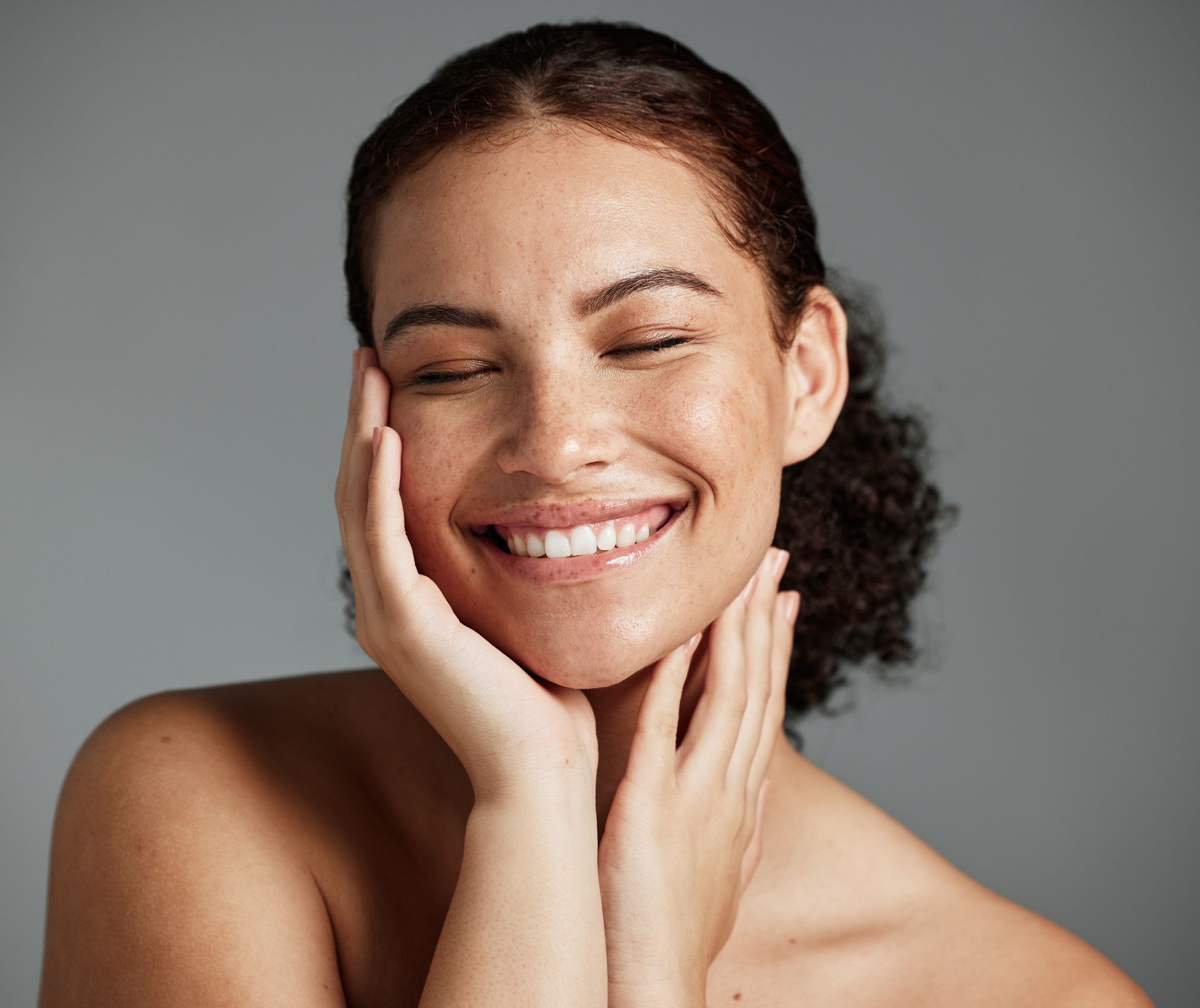 A woman is smiling with her eyes closed and her hand on her face. 
