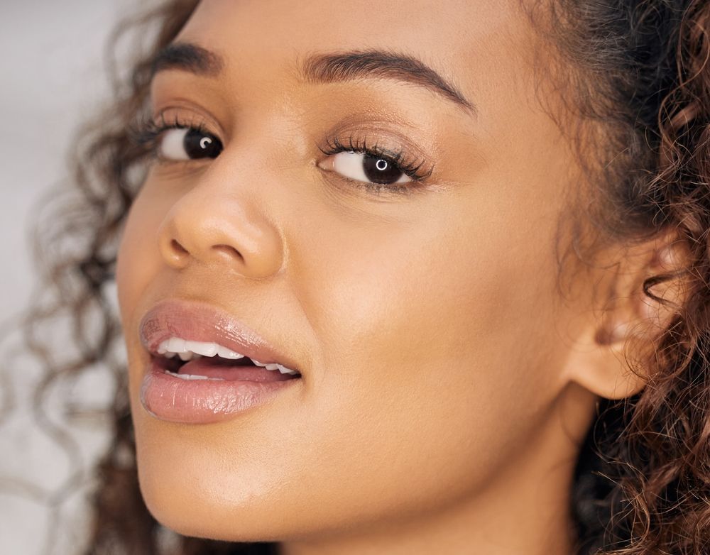 Close-up of a woman with curly brown hair and dark eyes, smiling and looking towards the viewer.