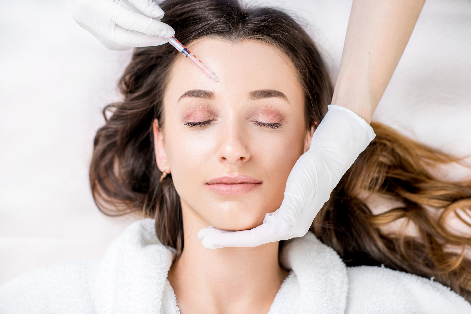 Gloved esthetician shaping a woman’s lips with a cosmetic procedure in a bright treatment room