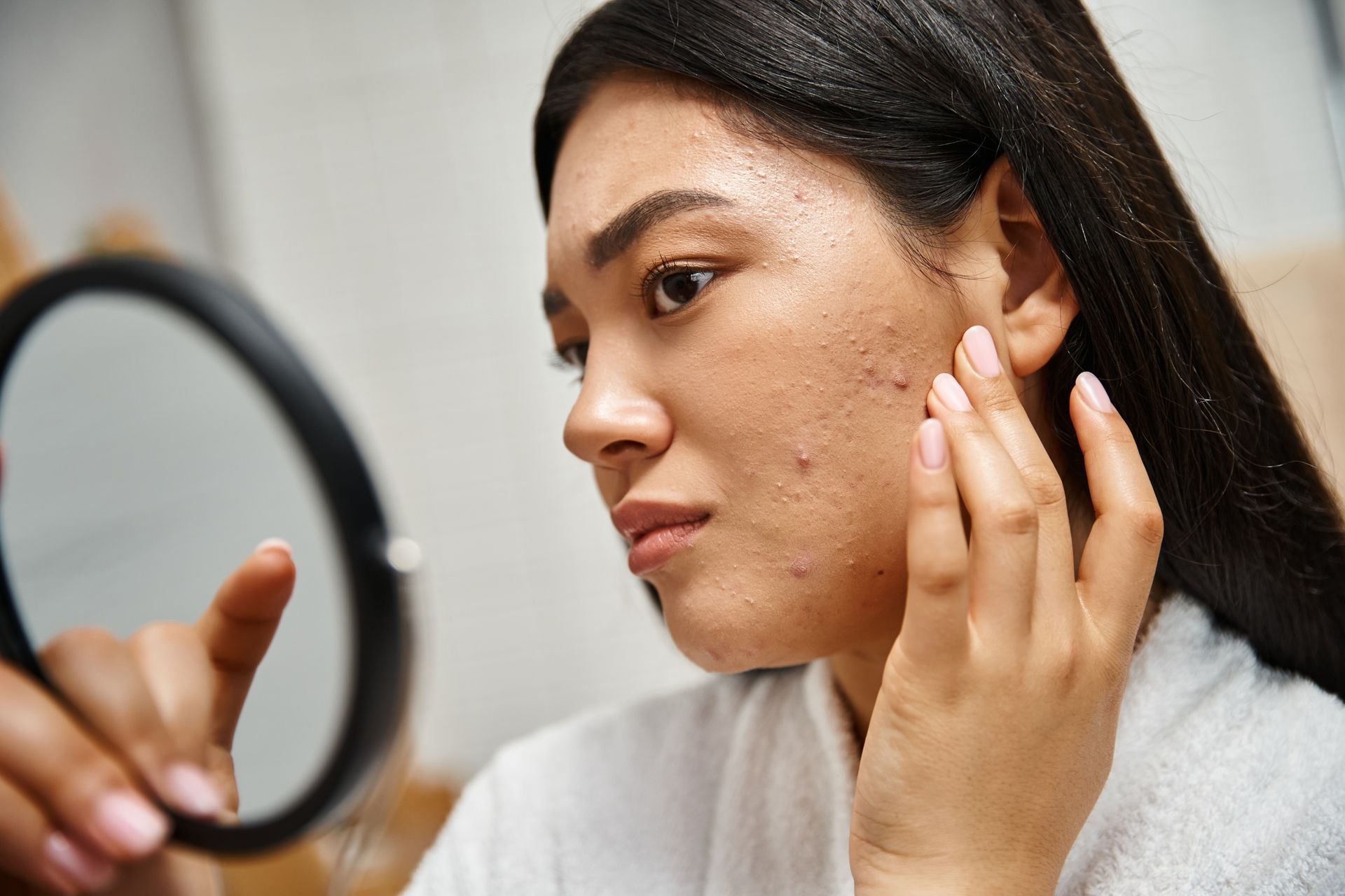 A woman is looking at her face in a mirror.