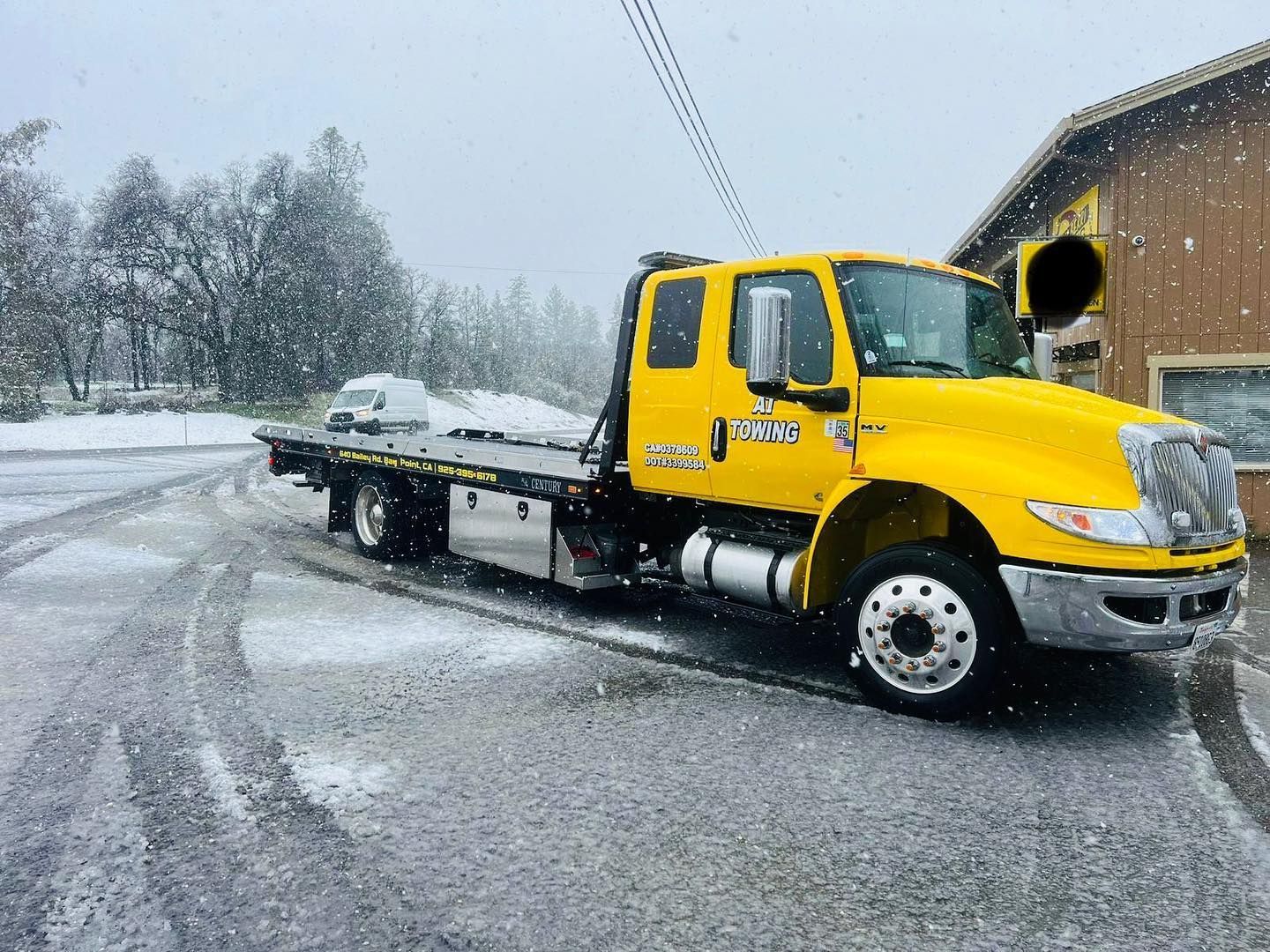 A yellow tow truck is parked on the side of the road in the snow.