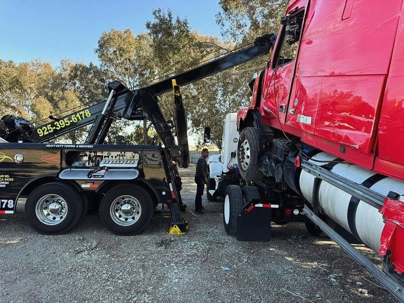 A red semi truck is being towed by a tow truck.