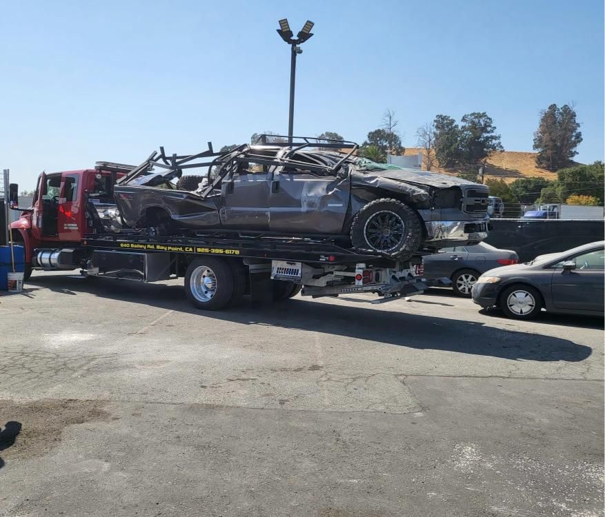 A tow truck is carrying a wrecked car in a parking lot