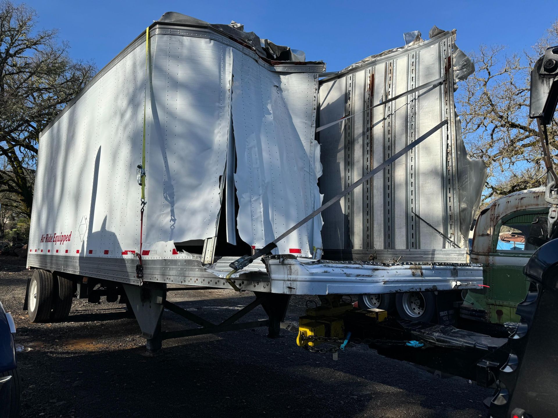 A white trailer with a broken side is parked in a parking lot.