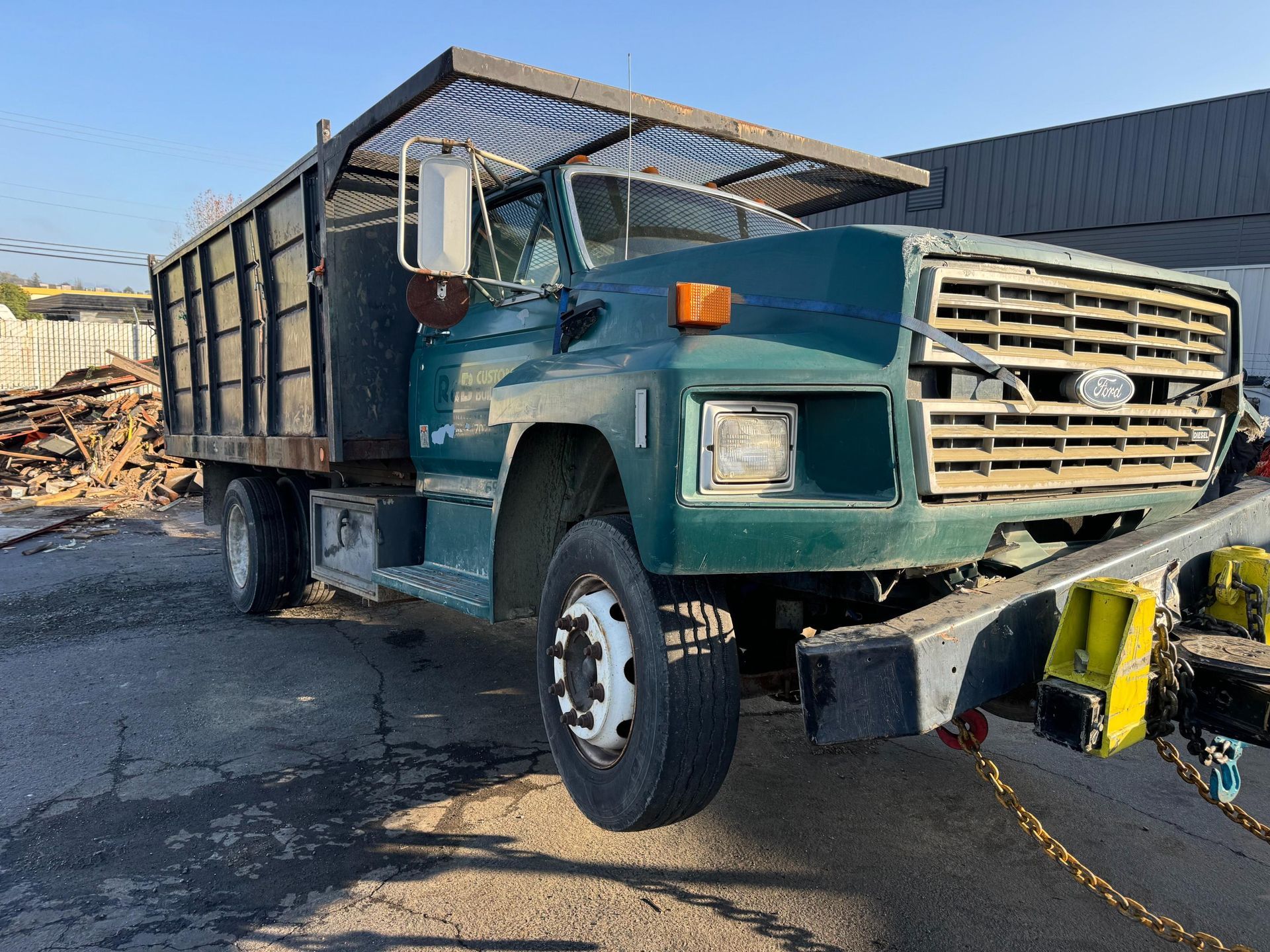 A green dump truck is parked in front of a pile of wood.