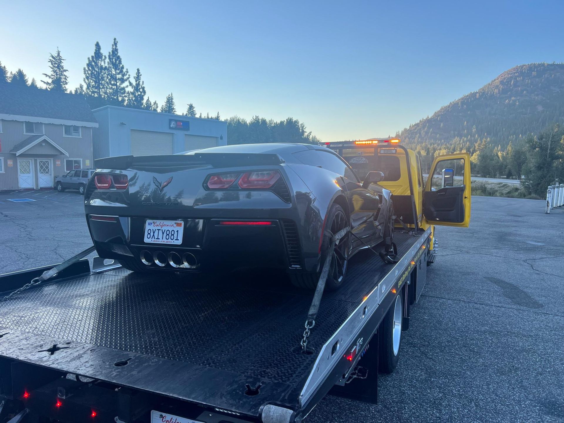 A black sports car is being towed by a yellow tow truck.