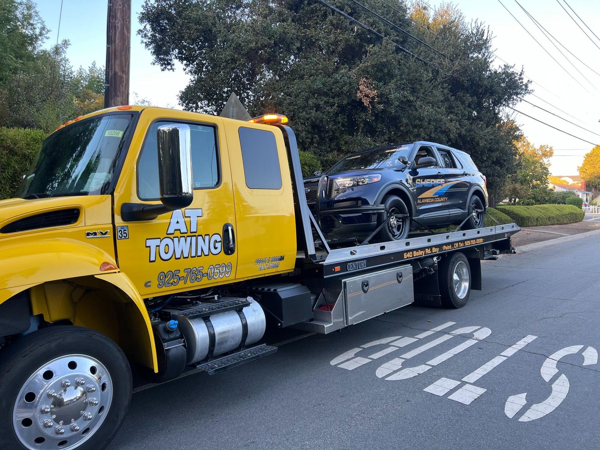A yellow towing truck is carrying a car on the back of it.