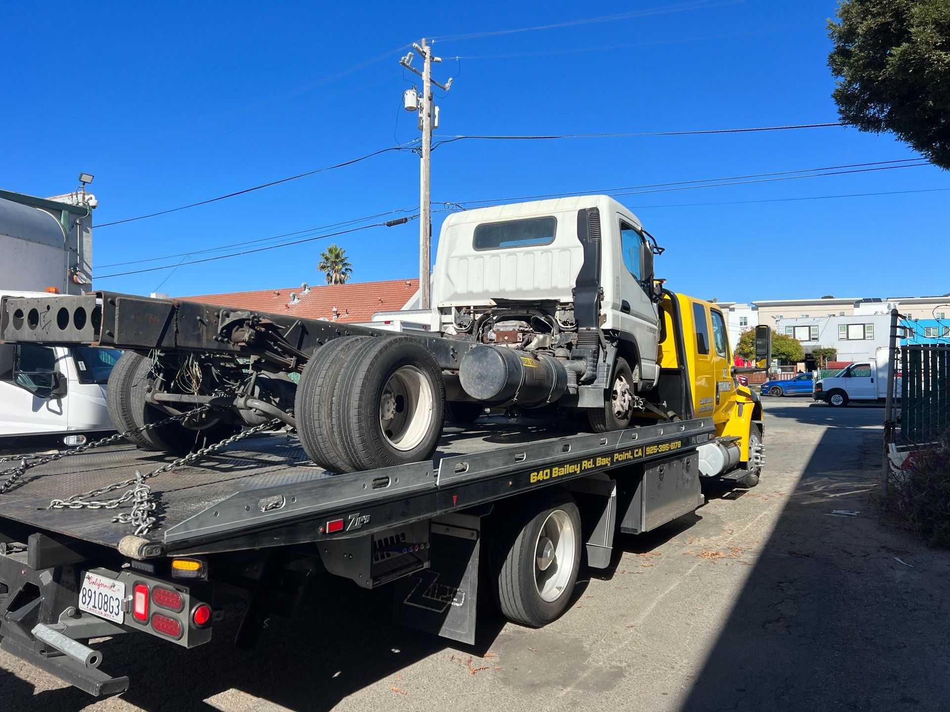 A yellow tow truck with a white truck on the back is parked on the side of the road.