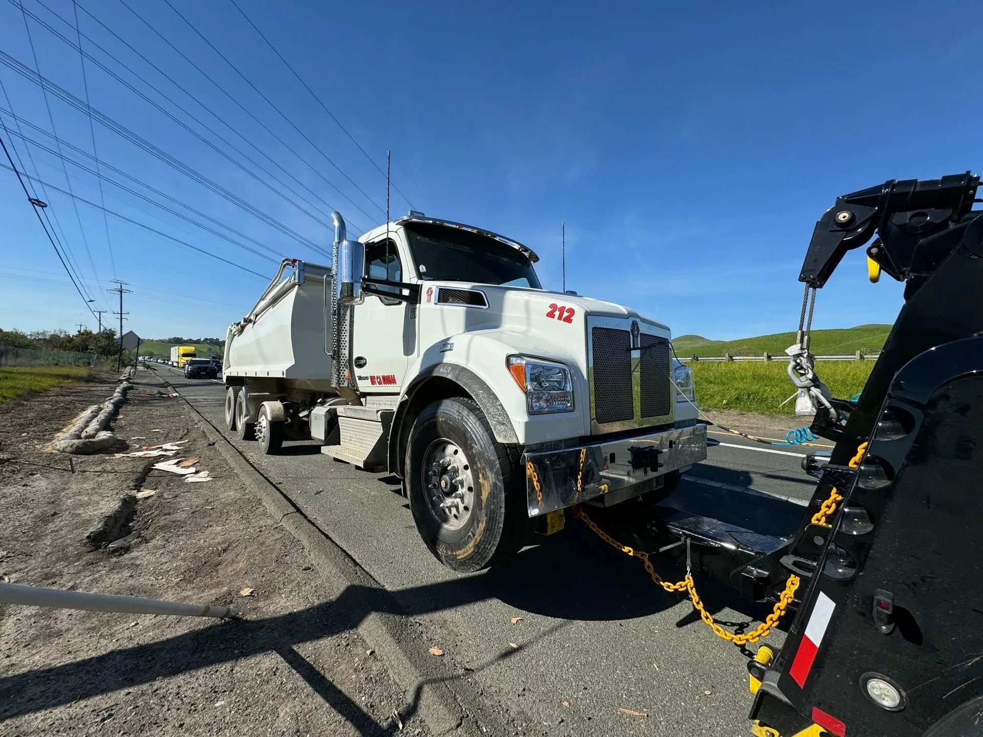 White dump truck being towed on a road with power lines overhead on a sunny day.