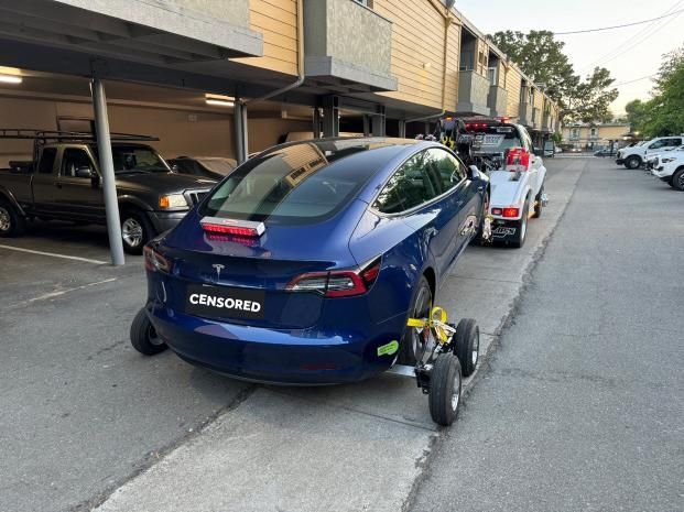 A tesla model 3 is being towed by a tow truck.