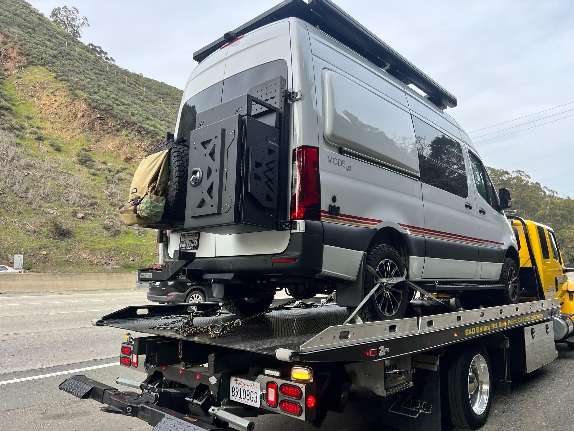 A van is being towed by a tow truck on the side of the road.