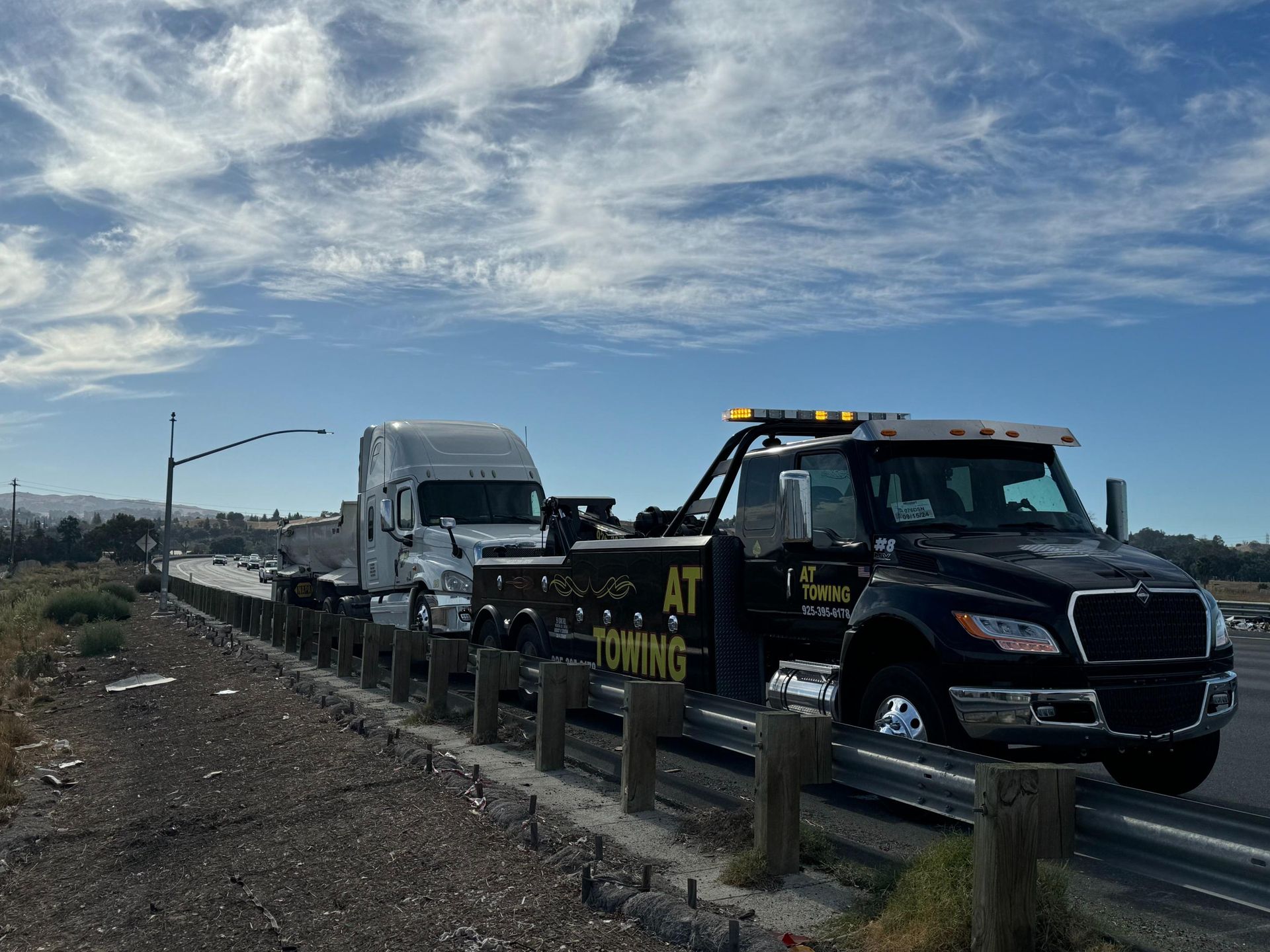 A tow truck is towing a semi truck on the side of the road.