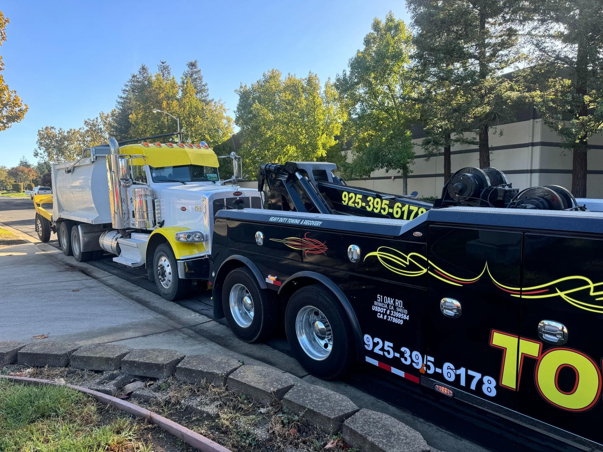 A tow truck is parked next to a dump truck on the side of the road.