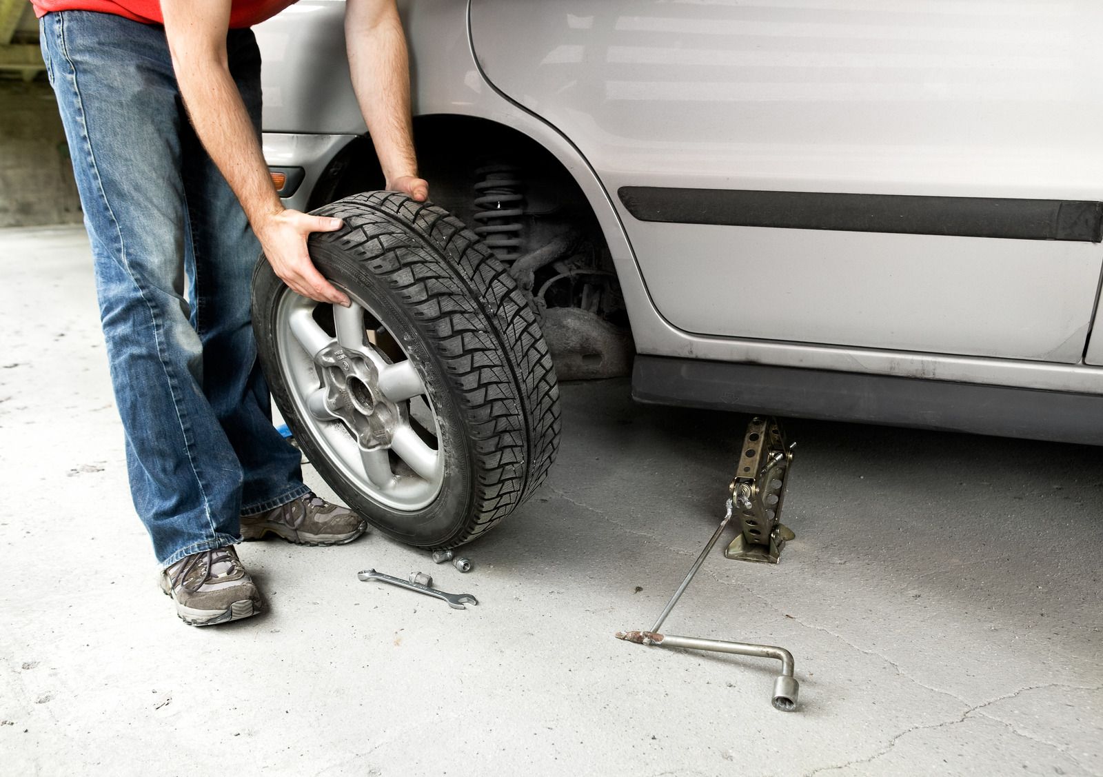 A man is changing a tire on a silver car.