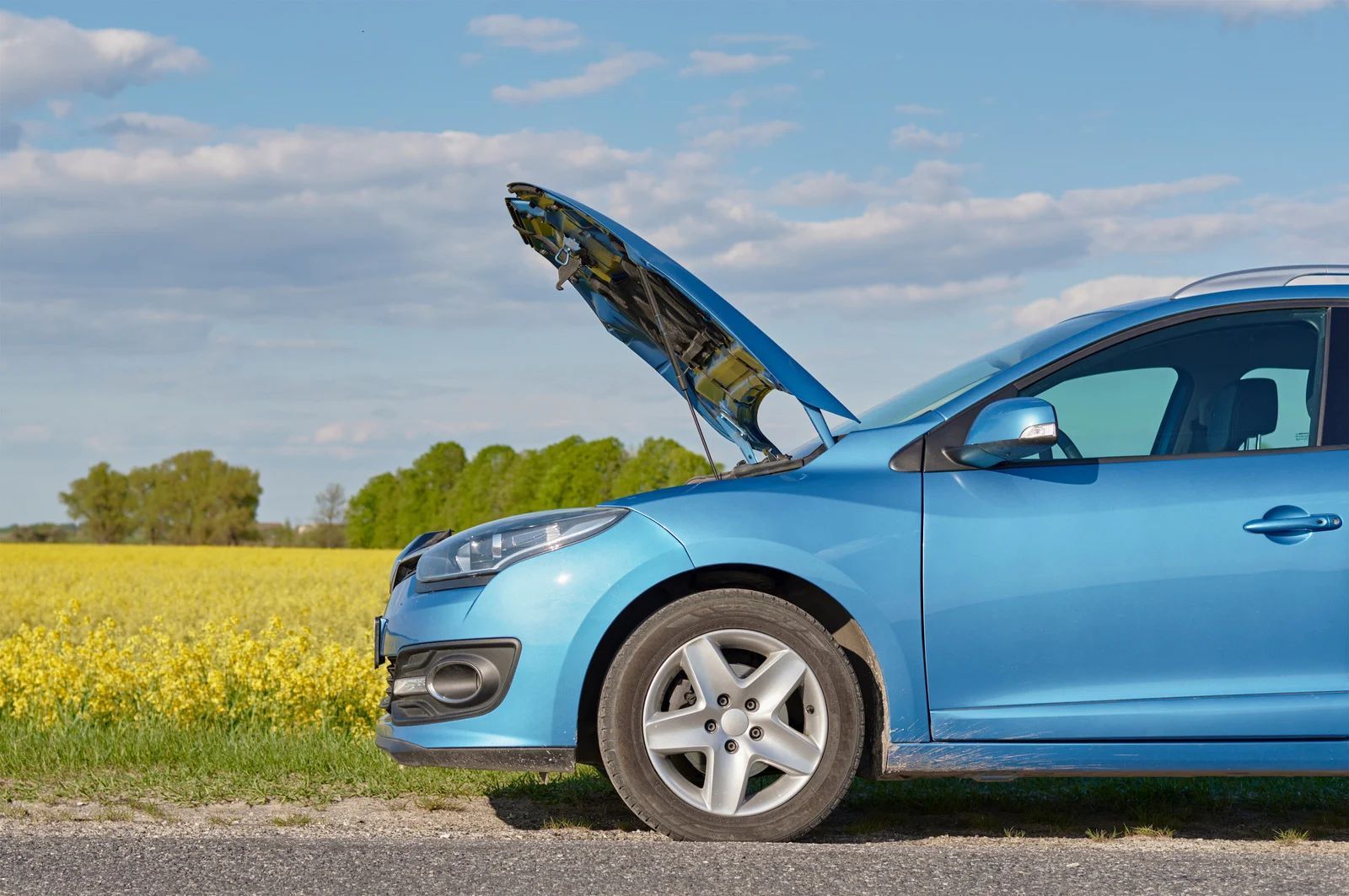 Blue car with open hood on roadside, next to a yellow field, under a cloudy sky.