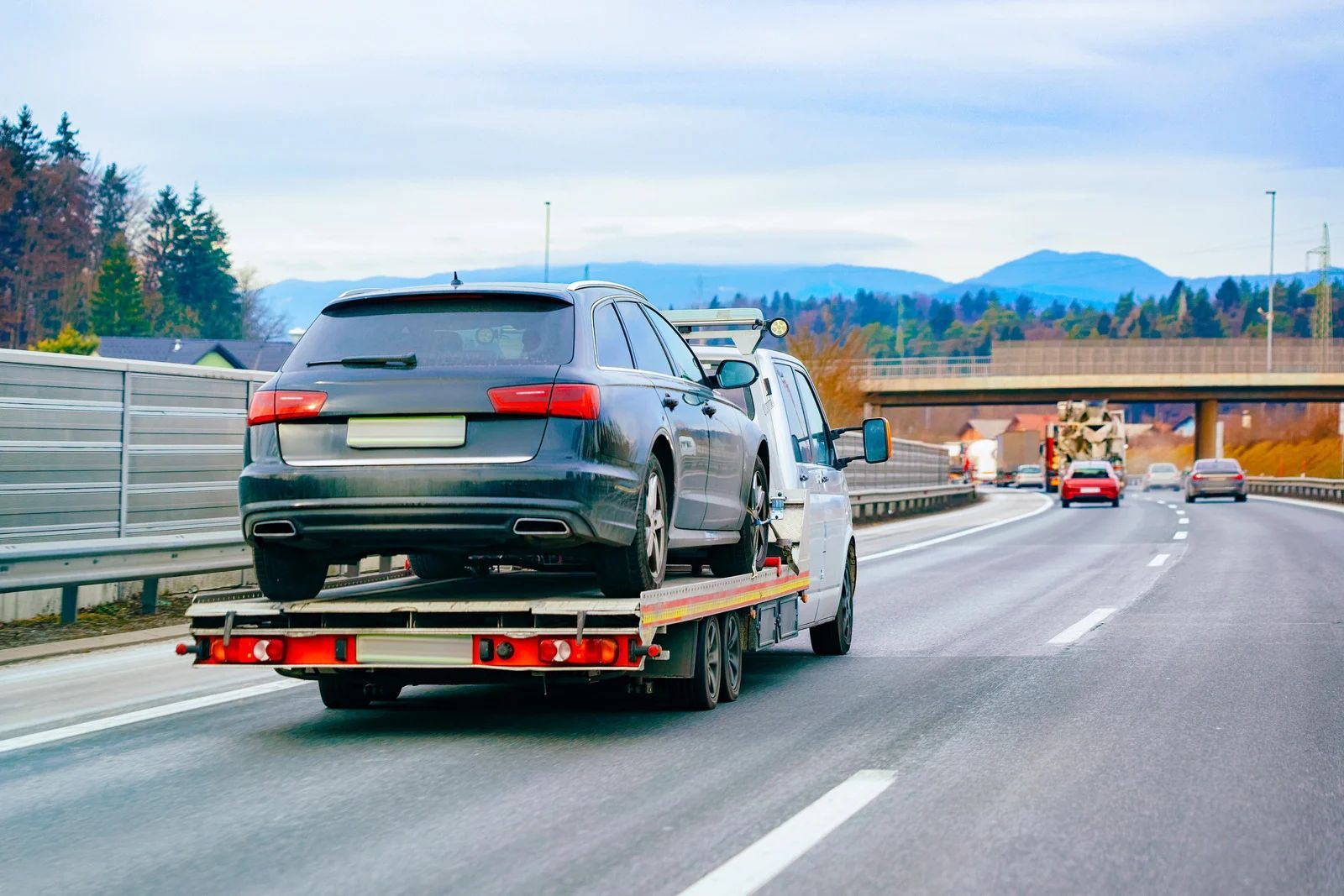 Tow truck hauling a black SUV on a highway under an overpass, with mountains in the distance