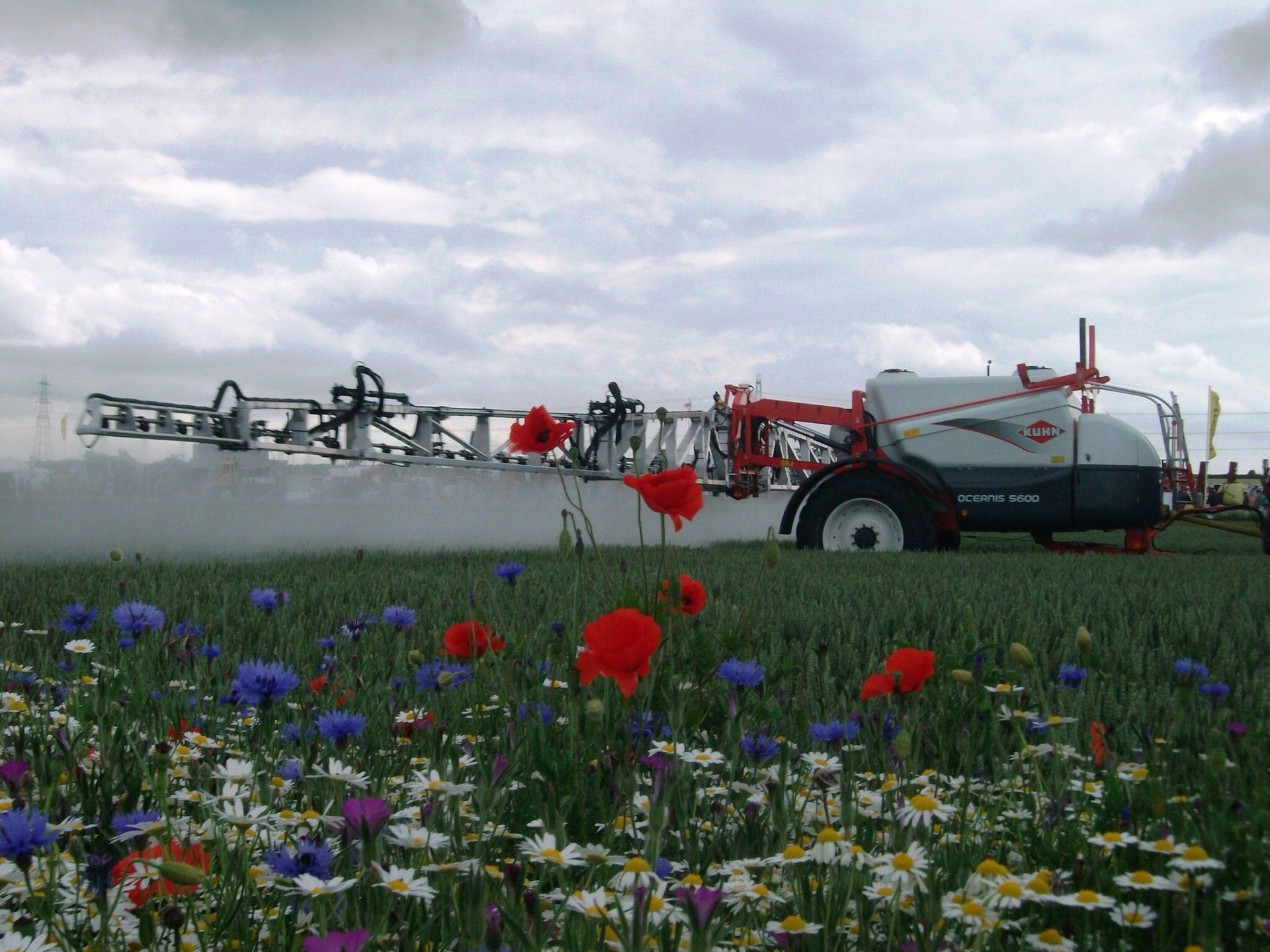 Un trattore che spruzza un campo di fiori con un cielo nuvoloso sullo sfondo
