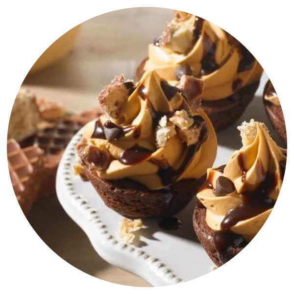 A white plate topped with cupcakes with peanut butter frosting and chocolate sauce