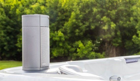 Gray hot tub speaker on white tub with green trees in background.