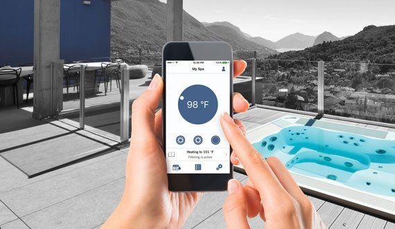 Person using a phone to control the temperature of a hot tub with a view of mountains.