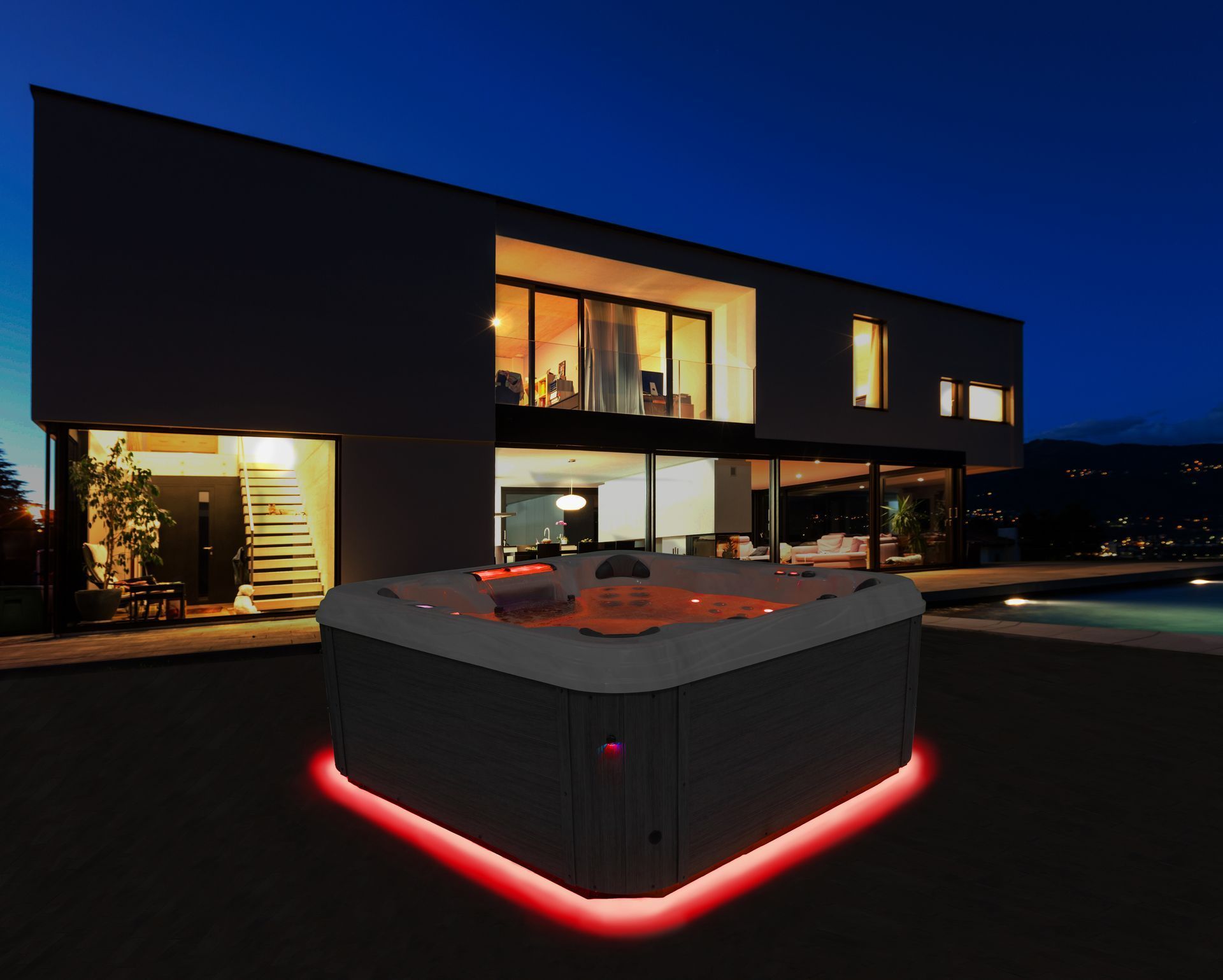 A square hot tub with red LED base lighting sits outside a modern, illuminated multi-story home at night.