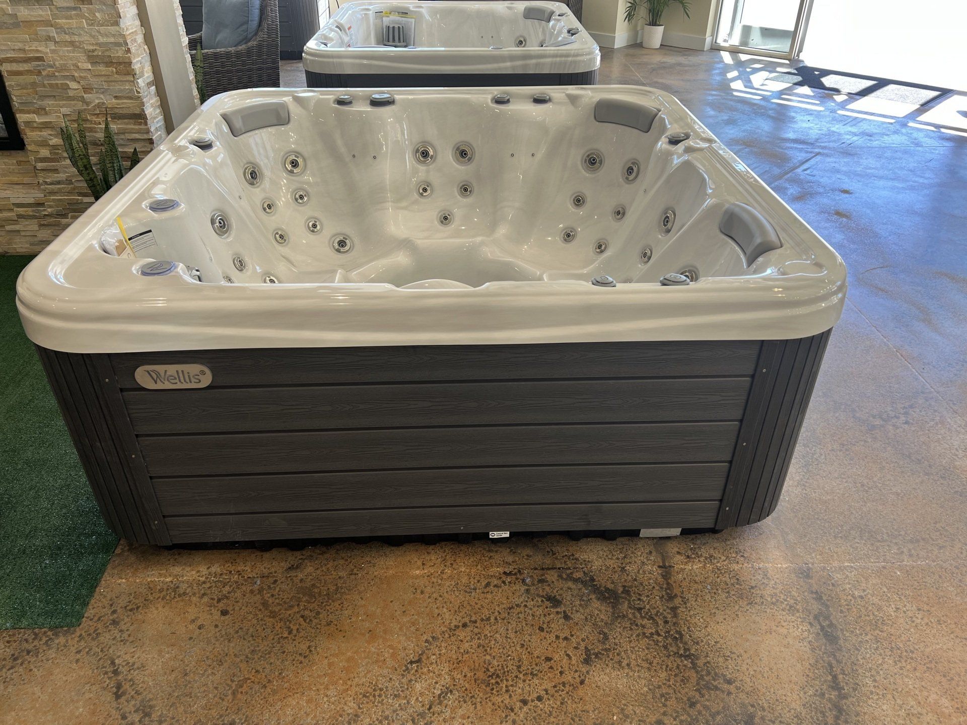 A square hot tub with gray exterior and white interior, displayed indoors on a polished floor.
