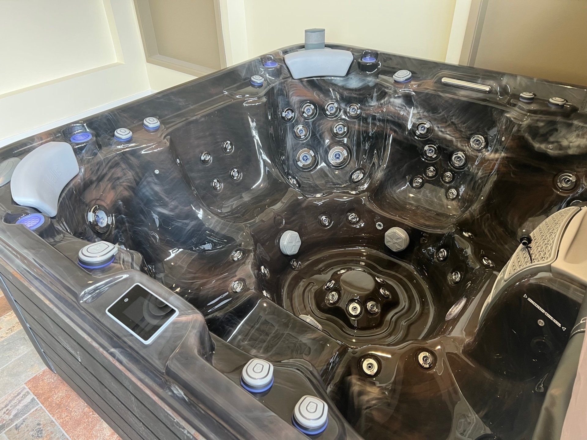 Dark-colored hot tub with multiple jets and control panel, in a room with beige walls.