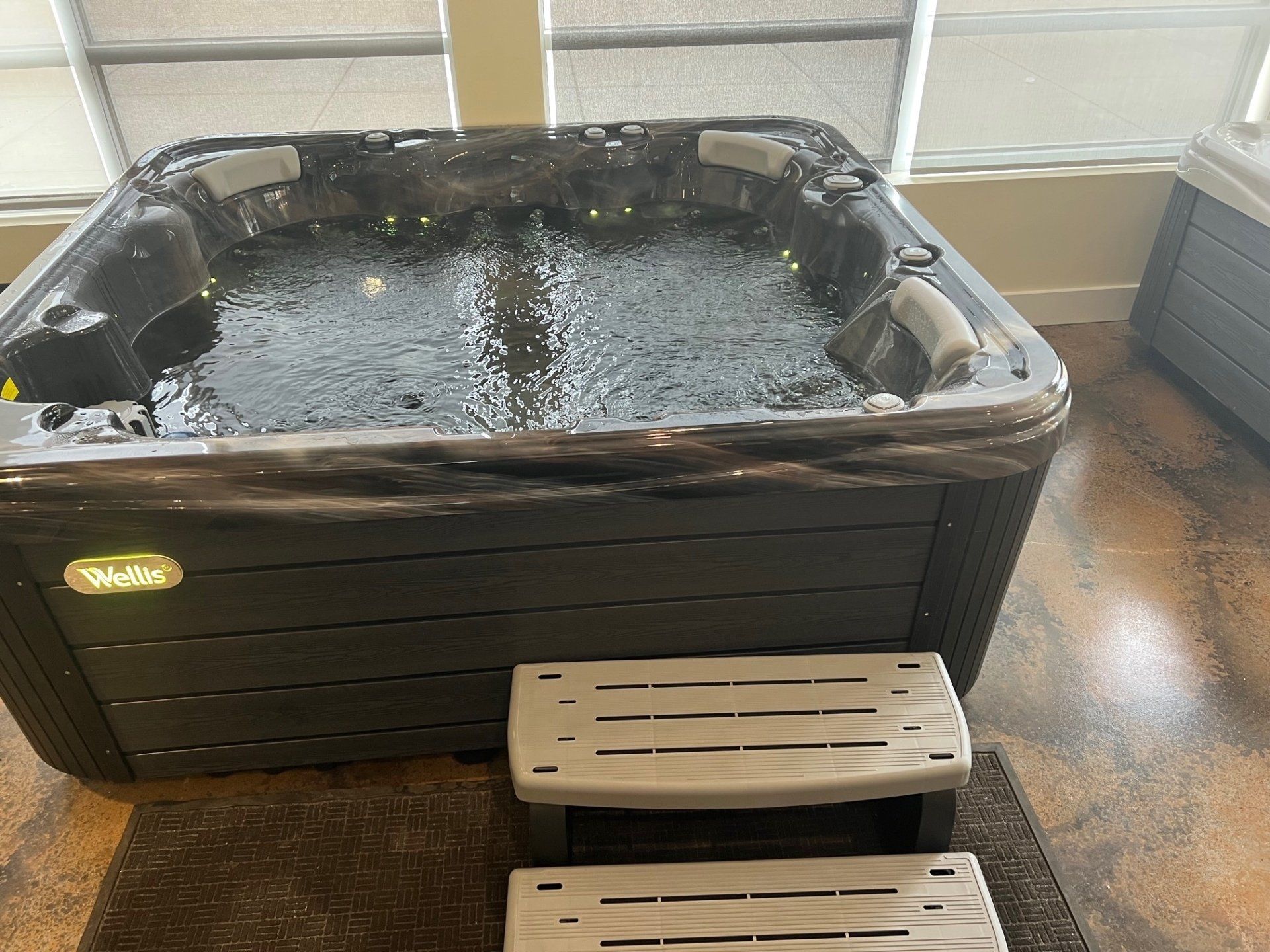 Hot tub with bubbling water and steps, set indoors with window view.