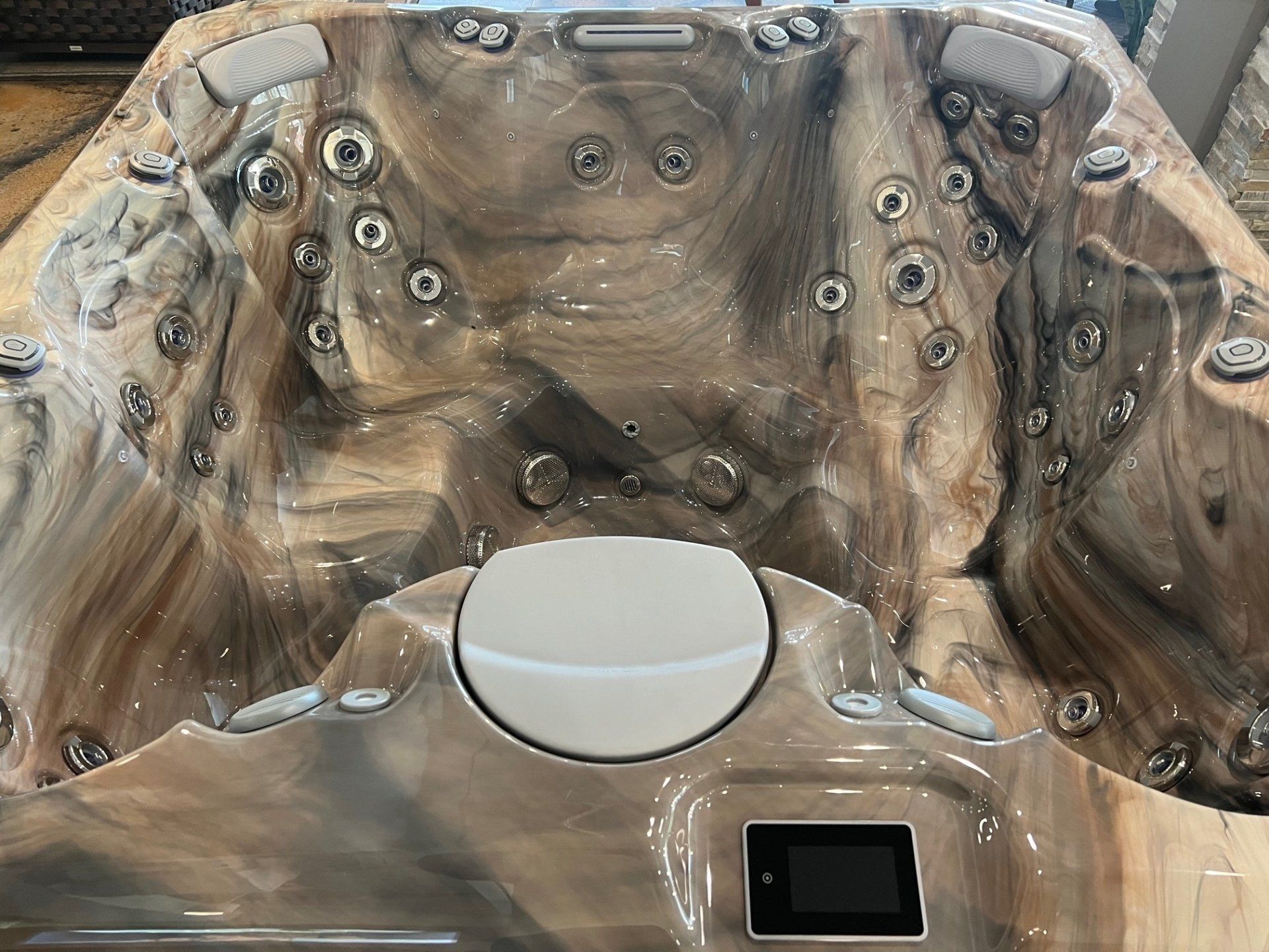 Hot tub interior with marbled brown and tan texture, jets, and digital control panel.